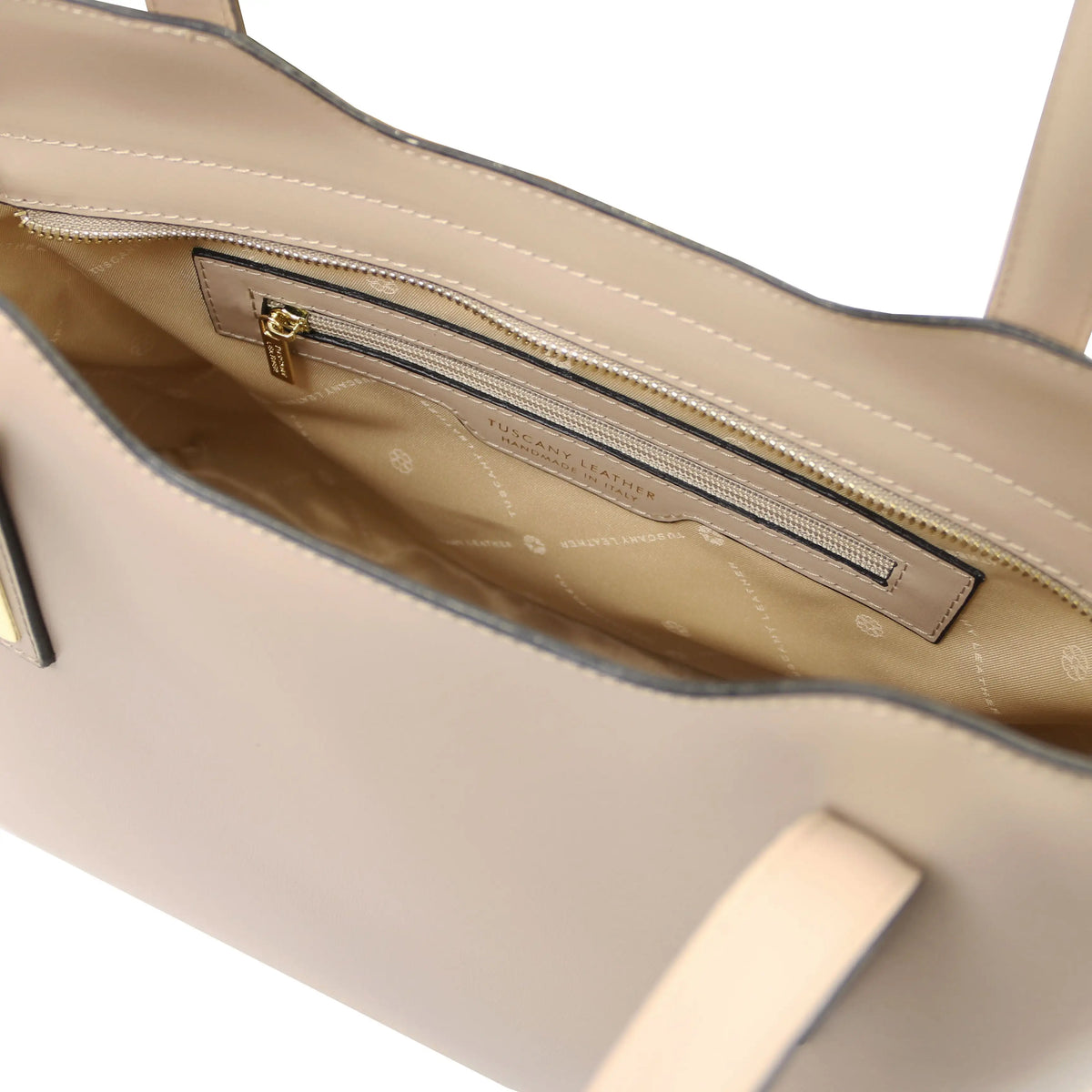 Close-up of the interior of a light taupe leather handbag, showing a zippered pocket with gold-tone hardware.