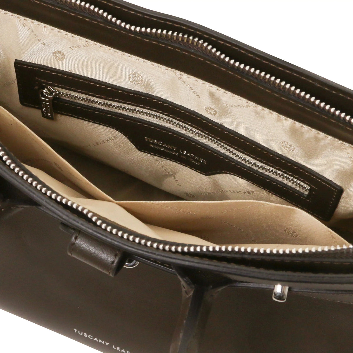 Close-up of the interior of a chocolate leather bag, showing a beige satin-lined compartment with a zip pocket and a visible Tuscany Leather brand label.