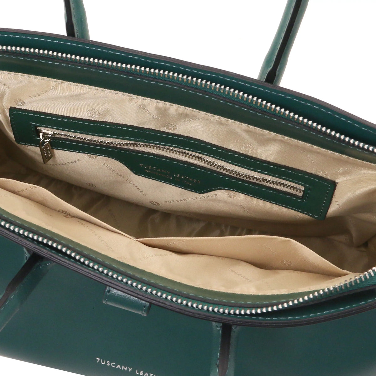 Close-up of the interior of a tealleather handbag, showing a beige patterned lining, a green interior zipper pocket with silver hardware, and the words 'TUSCANY LEATHER' printed on the exterior.