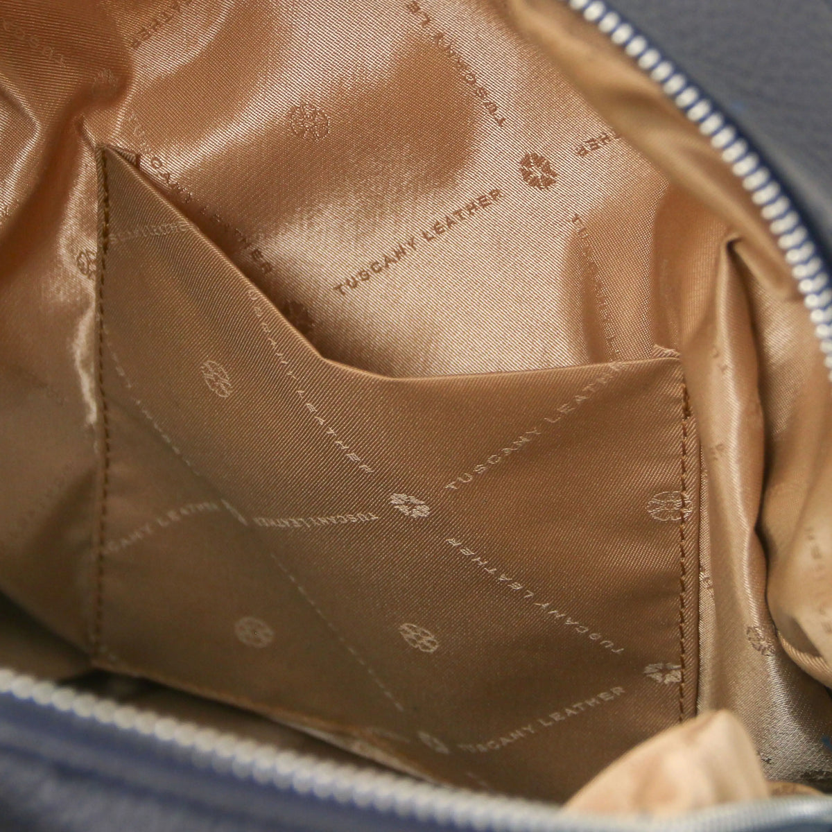 Close-up of the interior of a dark blue leather backpack showing a beige satin-lined open pocket and silver leather zipper trim