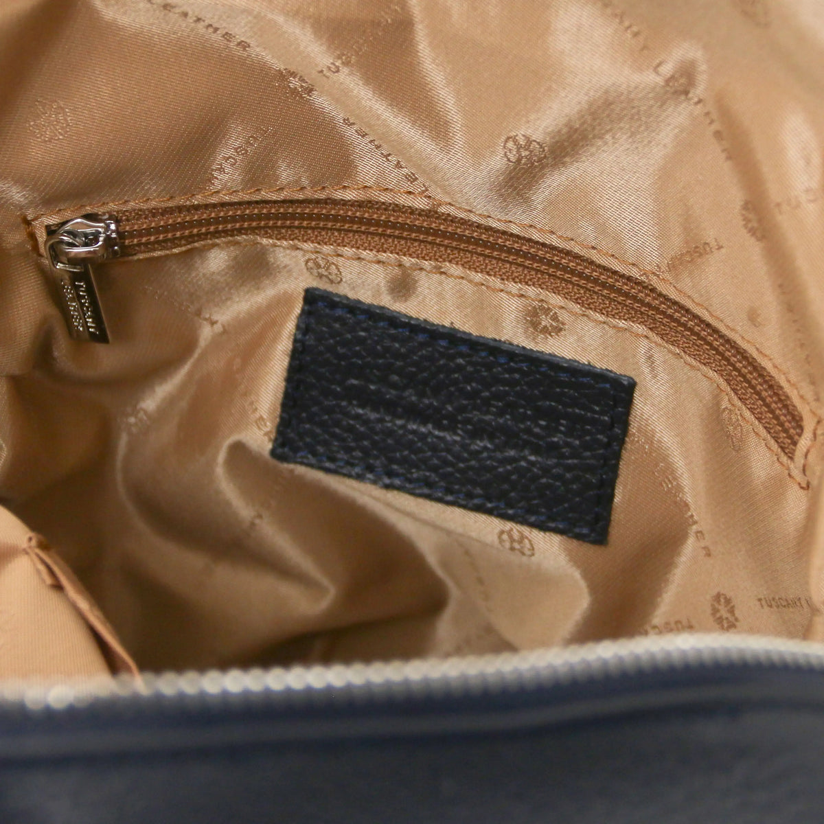 Close-up of a beige satin-lined interior pocket with a brown zipper, a dark navy textured label, and a silver-tone zipper