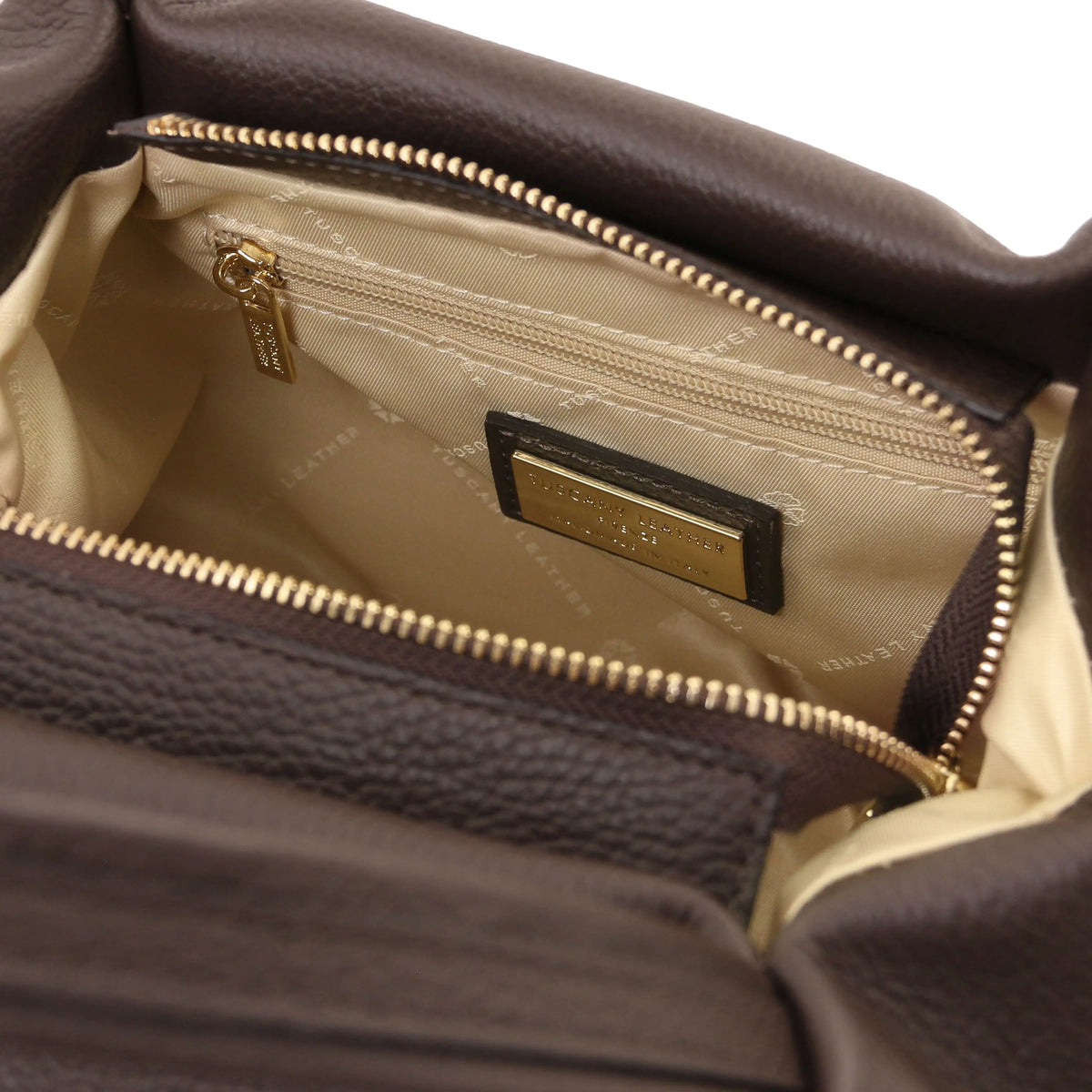 Close-up of a Chocolate textured leather handbag interior with gold-tone zippers and a beige branded lining. A gold-tone brand plaque and zipper pull read Michael Kors.