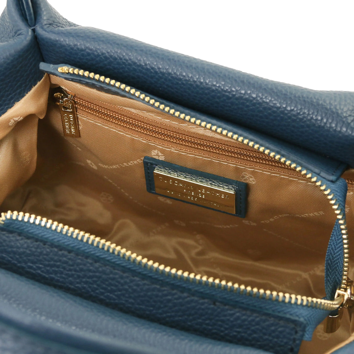 Close-up of an teal textured leather handbag showing the interior with a tan patterned lining, gold-tone zipper, and a blue leather brand plaque reading Michael Malul.
