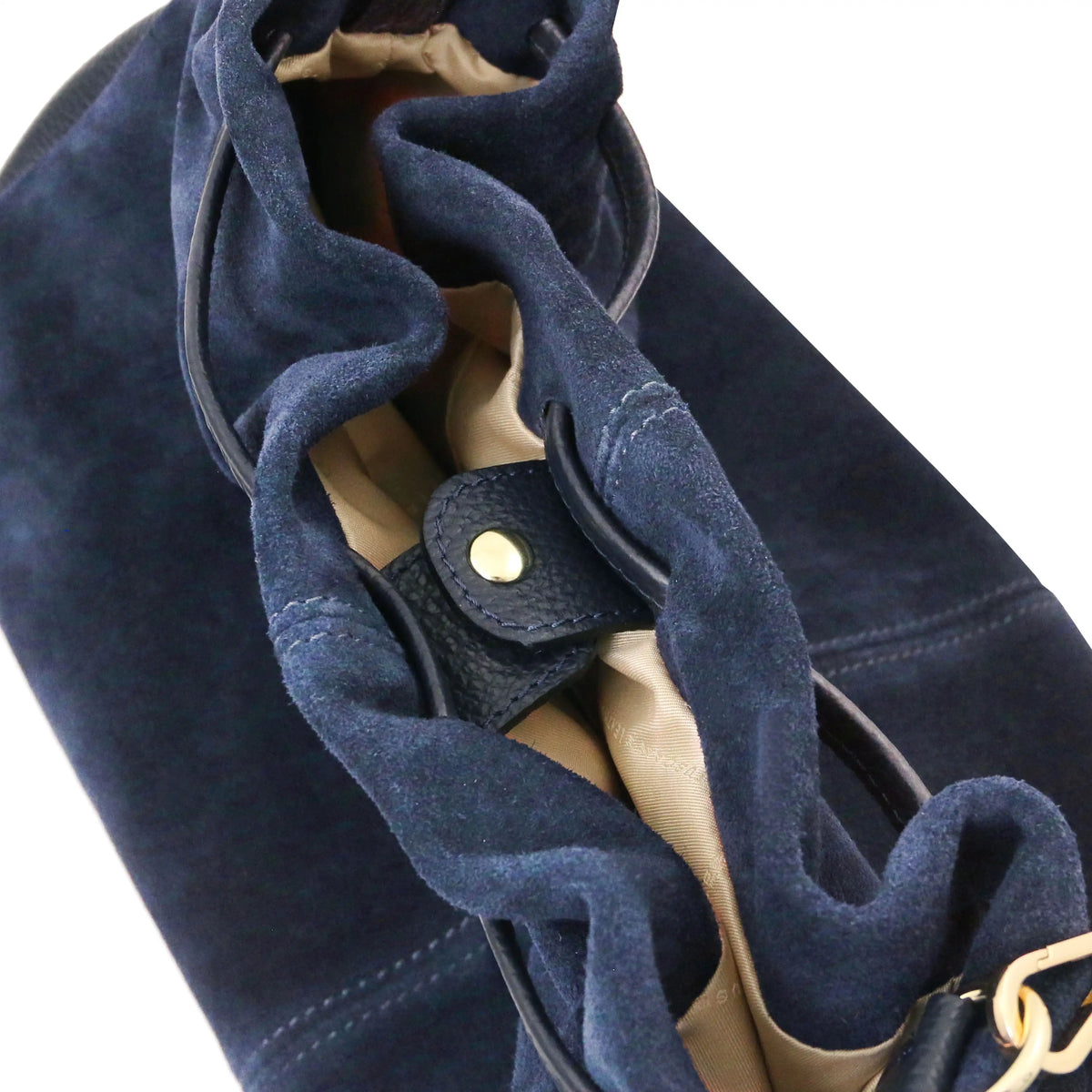 Close-up of a dark blue suede shoulder bag with a drawstring closure, beige interior lining, and a gold snap button.