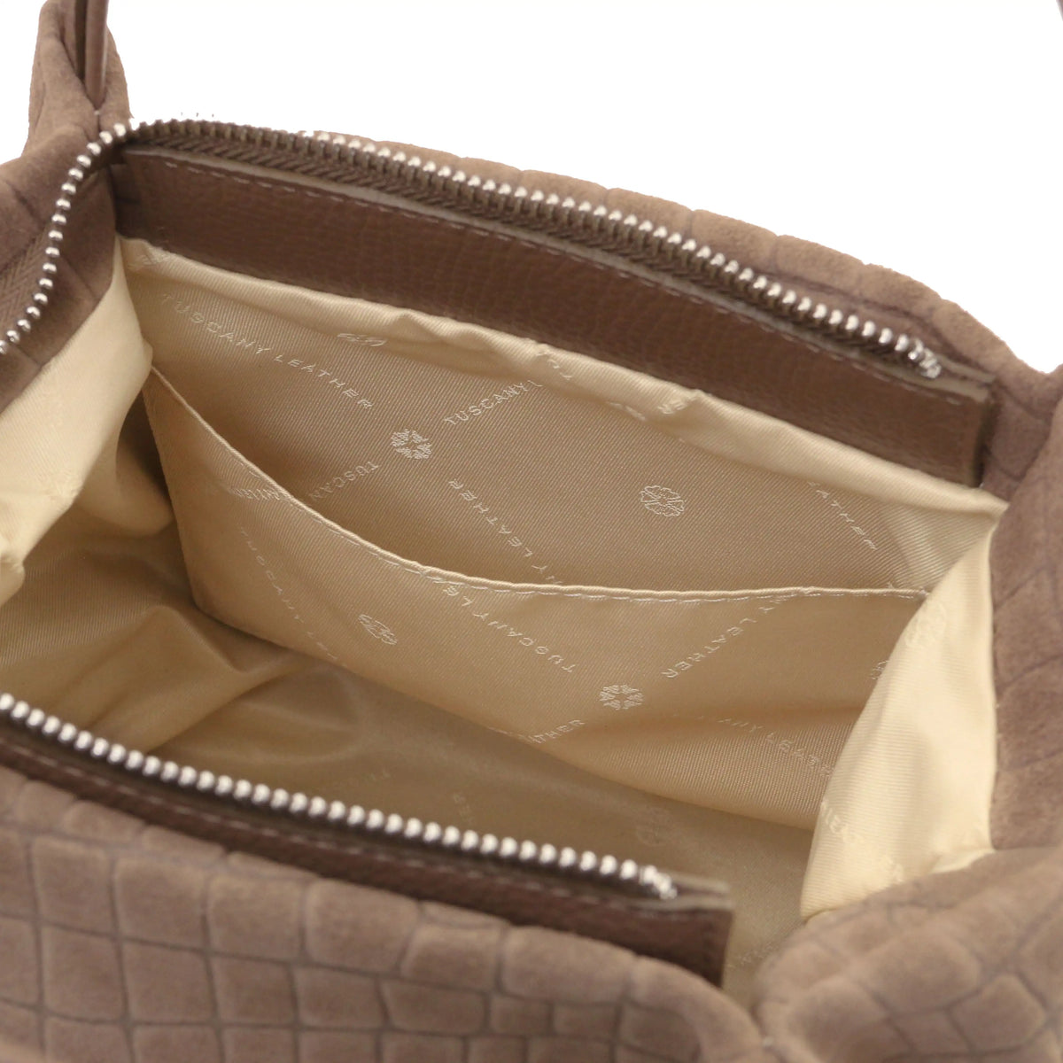 Close-up of the interior of a taupe croc textured leather bag, showing a cream-colored lining with a zippered pocket and silver zipper teeth.