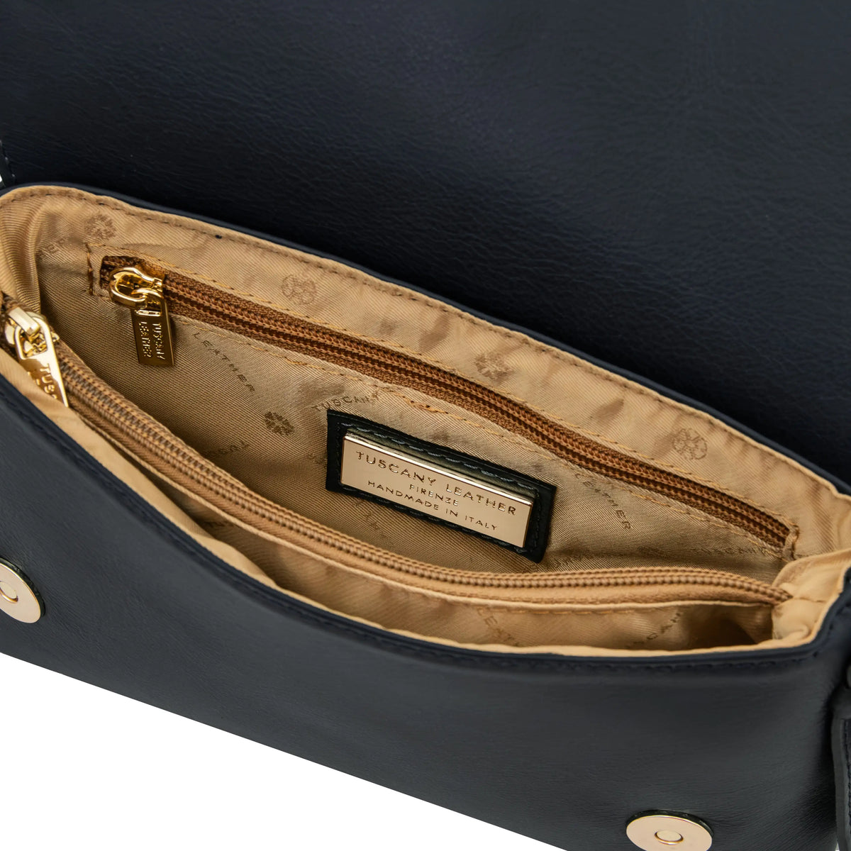 Close-up of a navy blue leather handbag interior showing a gold-toned zipper pull, zip pocket , beige lining, and visible Tuscany Leather branding.