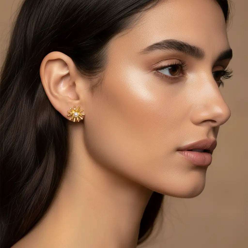 A close-up side profile of a woman with dark hair wearing a small gold flower-shaped stud earring against a warm beige background.