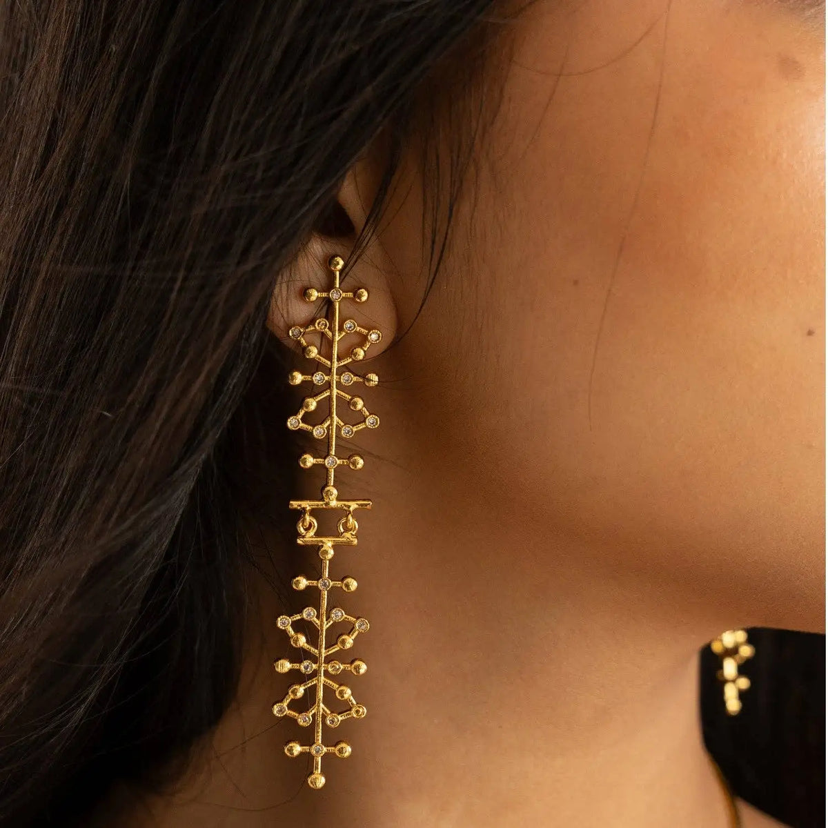 Gold statement earrings with an intricate, branching dendritic pattern and small clear cz accents being worn on a women's right ear