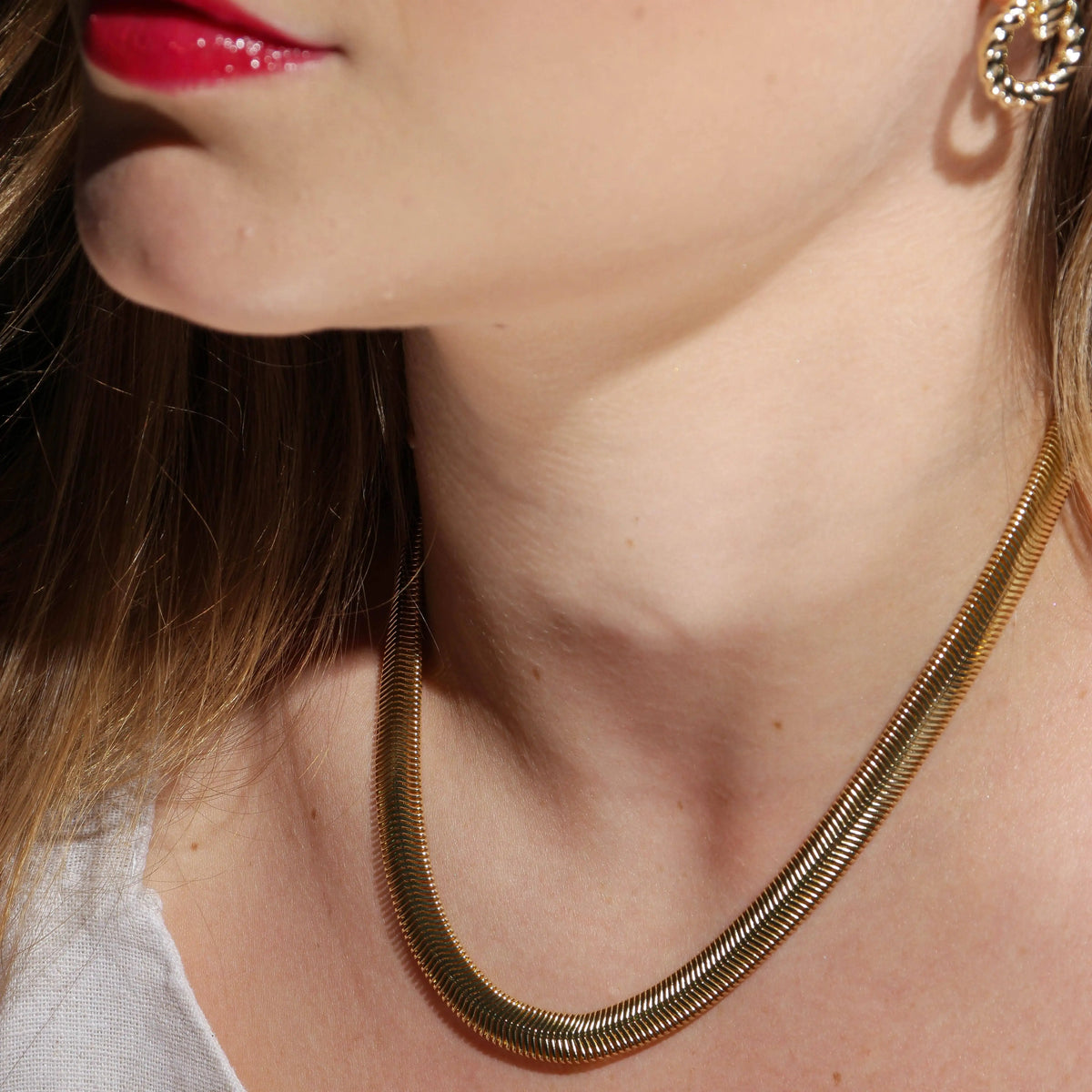 Close-up of a person wearing a gold 18" snak chain necklace and earring.