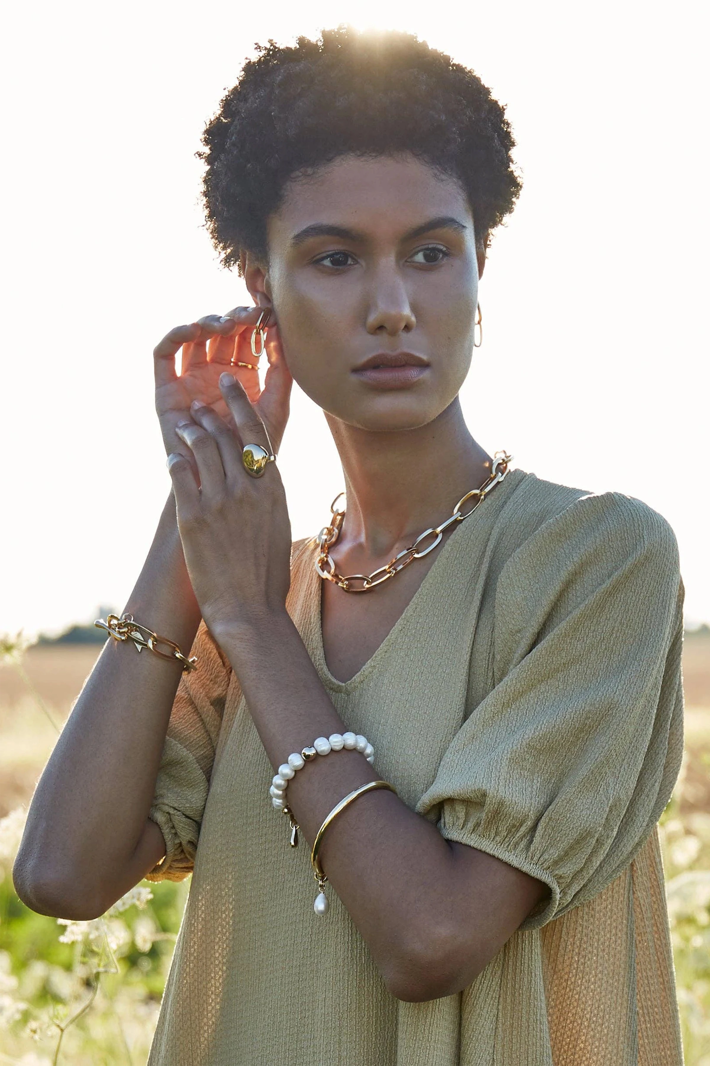 Woman in a field wearing gold chain jewelry with a blurred natural background