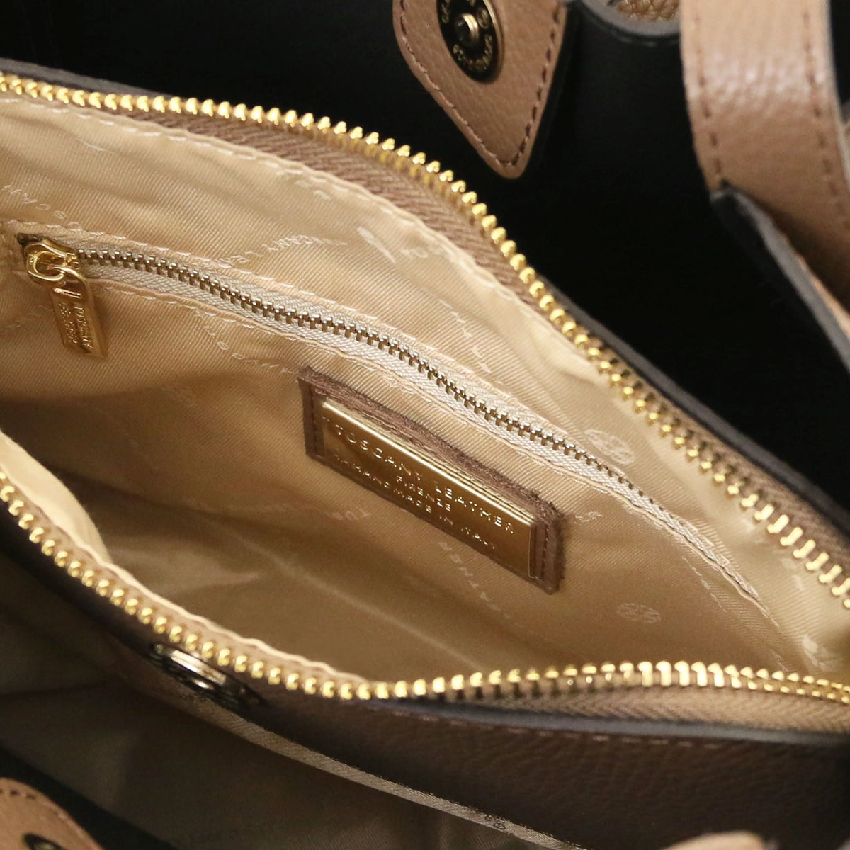 Close-up of the interior of a handbag showing a beige patterned fabric lining, gold-tone zippers, and a metal brand plaque that reads 'Celine'.