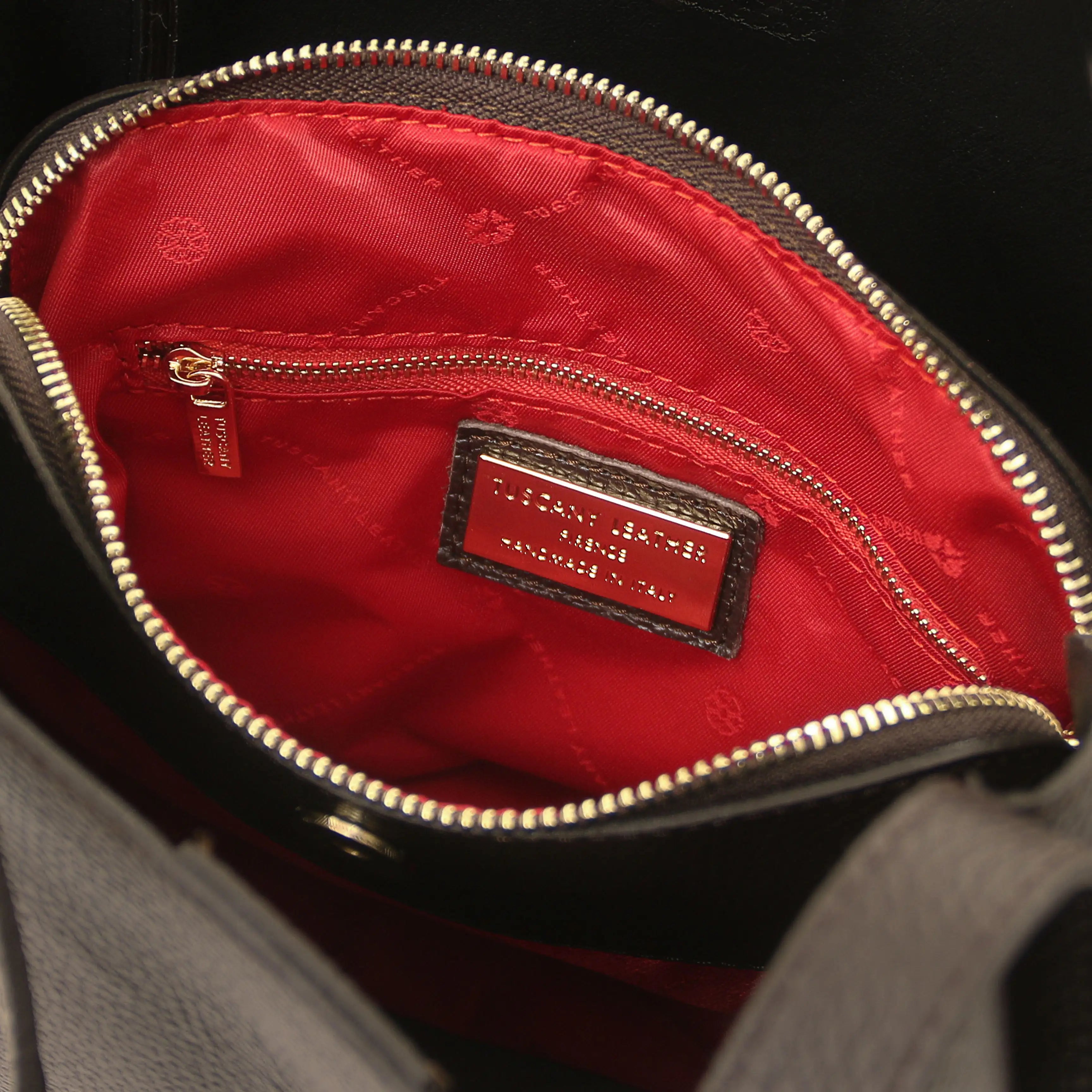 Close-up of a black leather handbag interior with a bright red quilted lining, gold-tone zipper, and a visible Michael Kors brand patch.