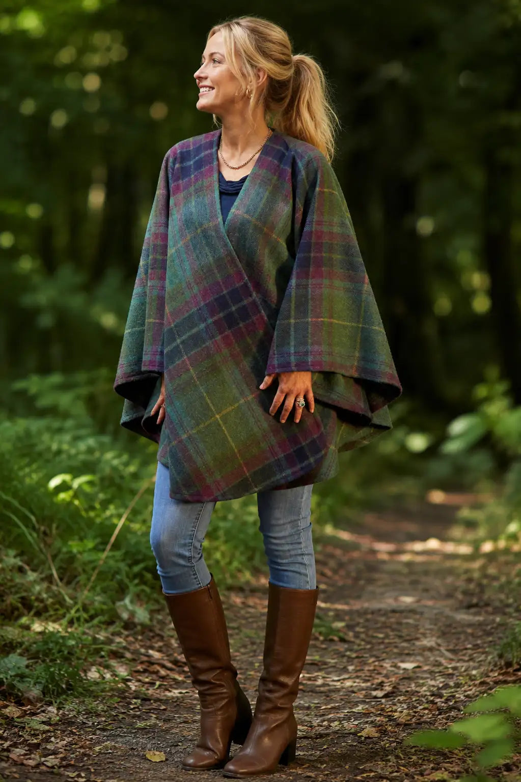Woman wearing Irish Emerald Isle Tartan Ruana Wrap and brown boots in a forest setting