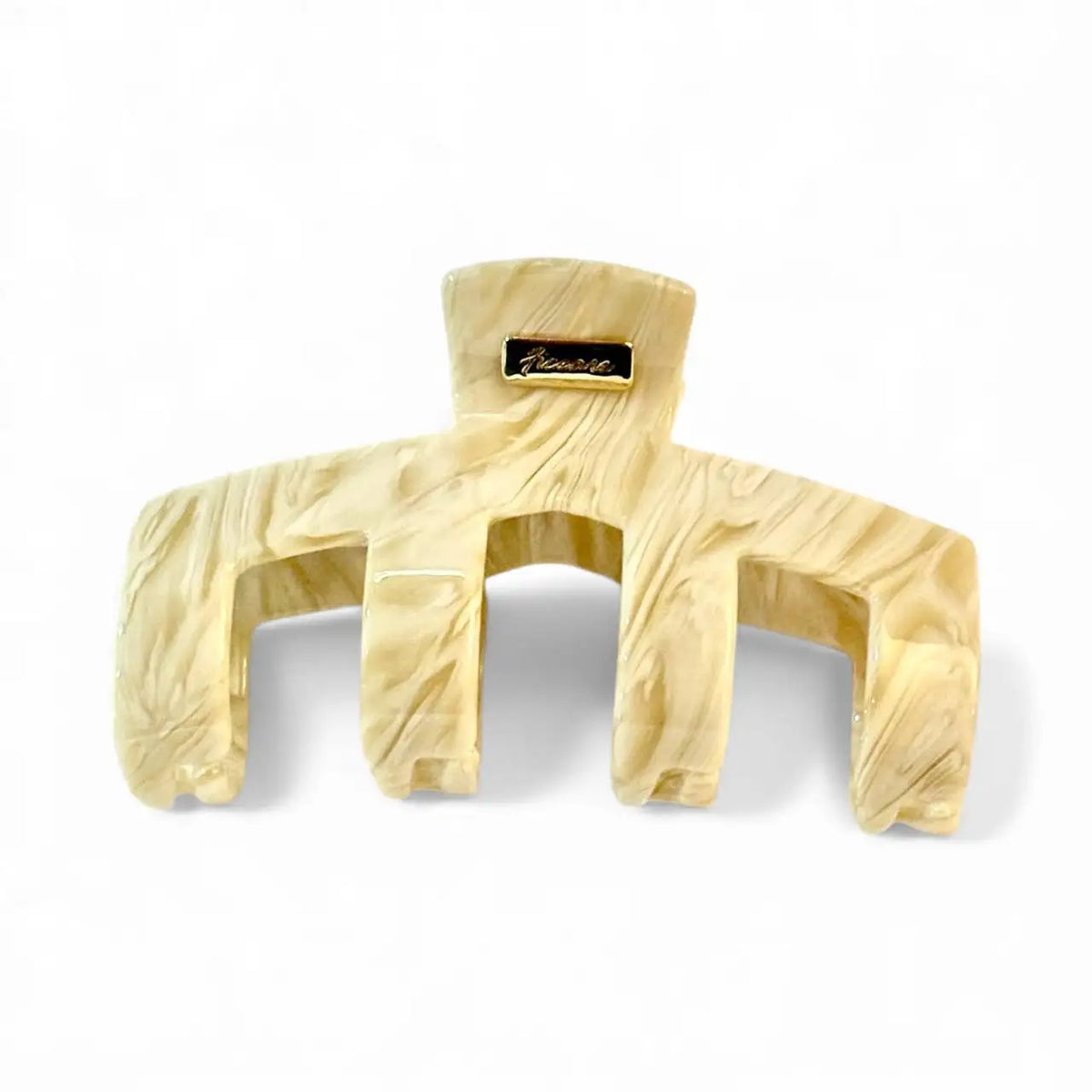 A large hair claw clip in a light cream or ivory acetate with a subtle marbled swirl pattern and a small gold-tone brand plaque at the top, shown on a clean white background.