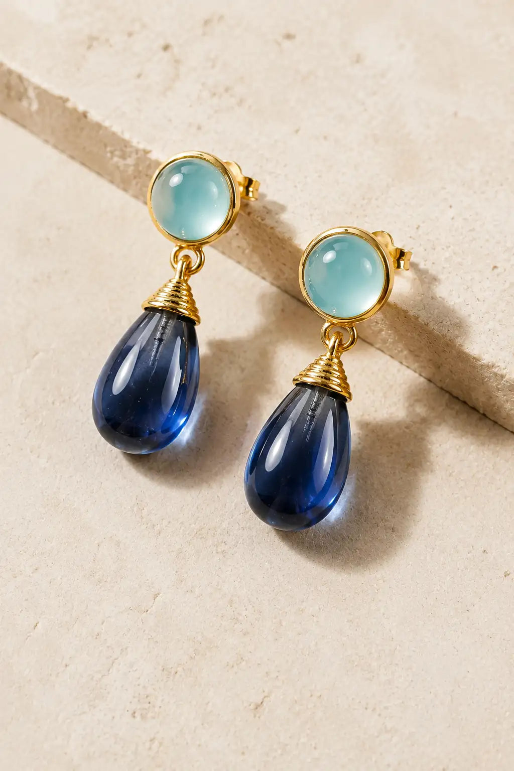 Nevaeh Drop Earrings Aqua Chalcedony & Blue Iolite with 18K gold accents laying on a stone background