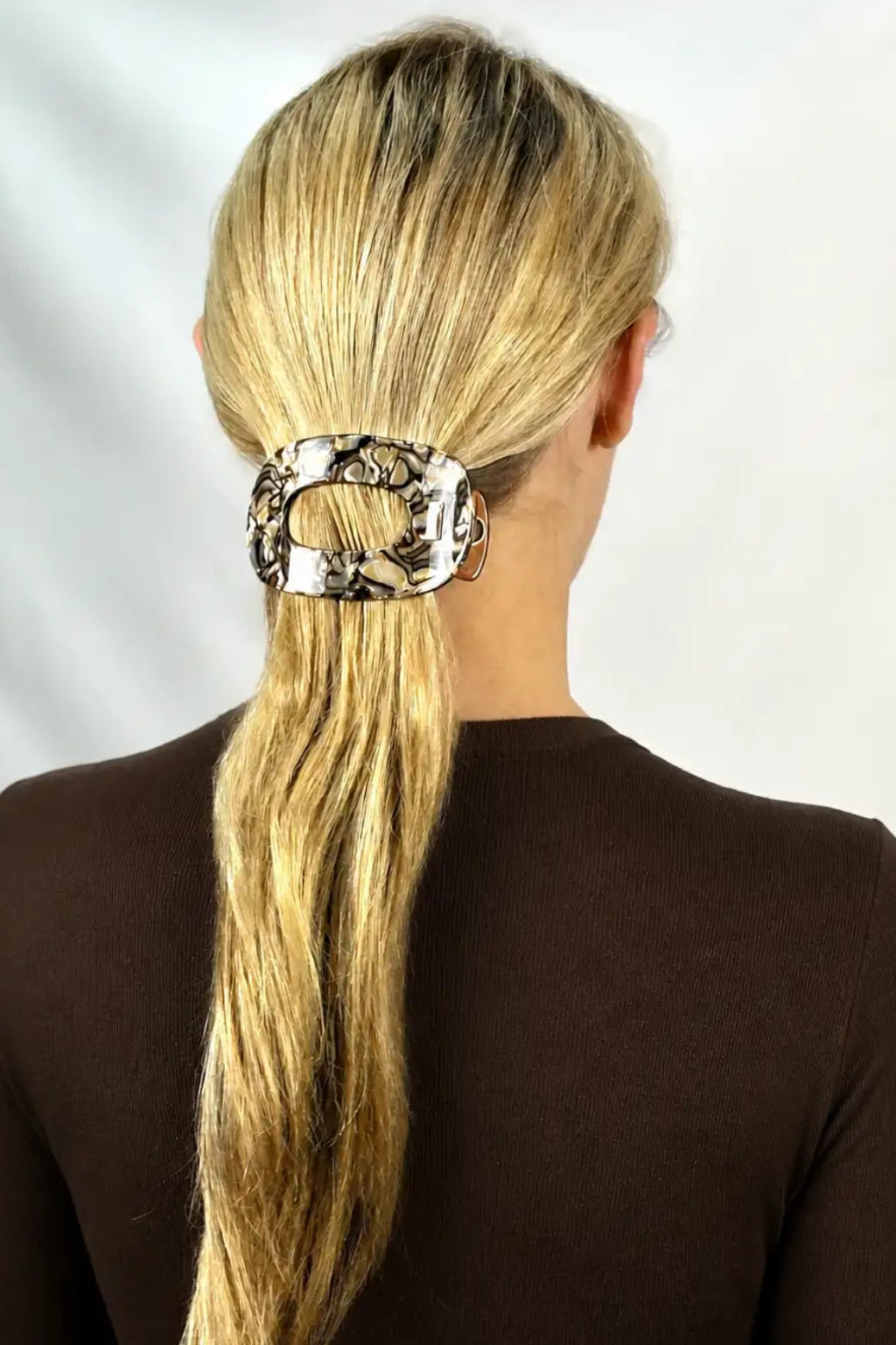 A woman viewed from the back wearing a brown swirl pattern flat hair claw clip holding her blonde ponytail.