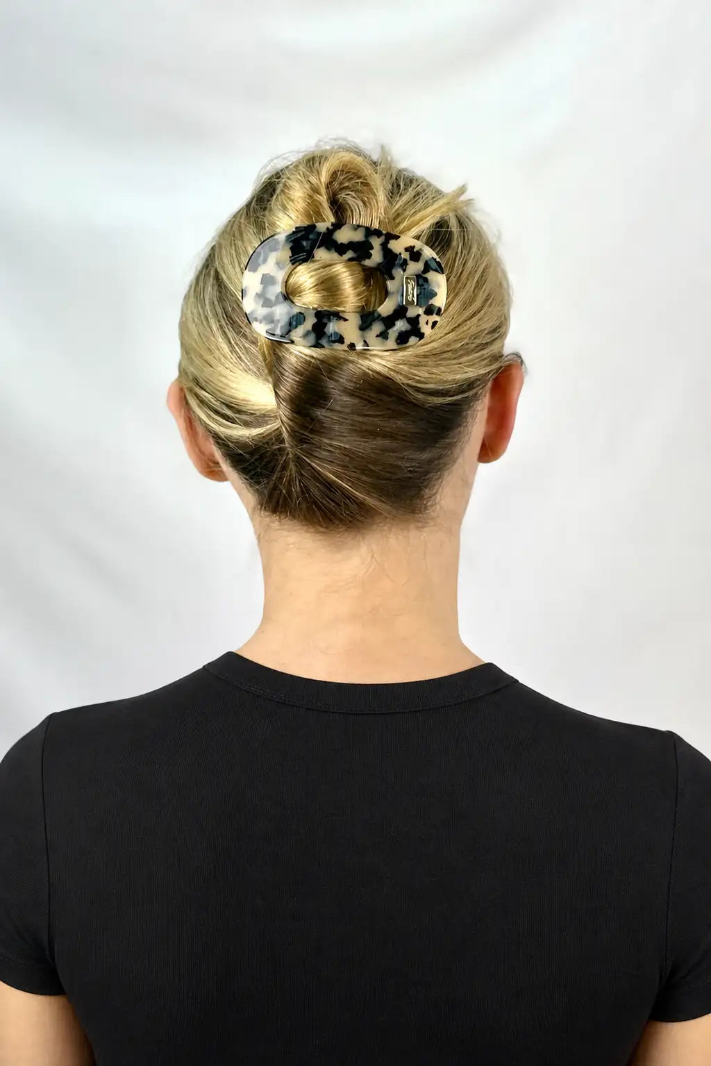 A woman shown from the back wearing a leopard-print hair claw clip to hold up a bun, against a plain light background.