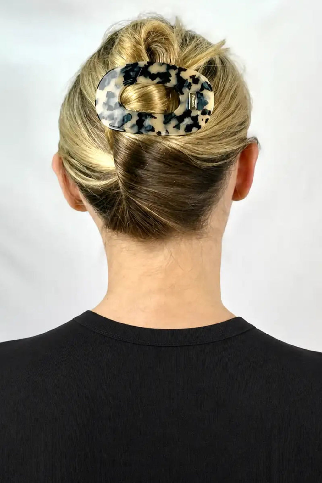 A woman shown from the back wearing a leopard-print hair claw clip to hold up a bun, against a plain light background.