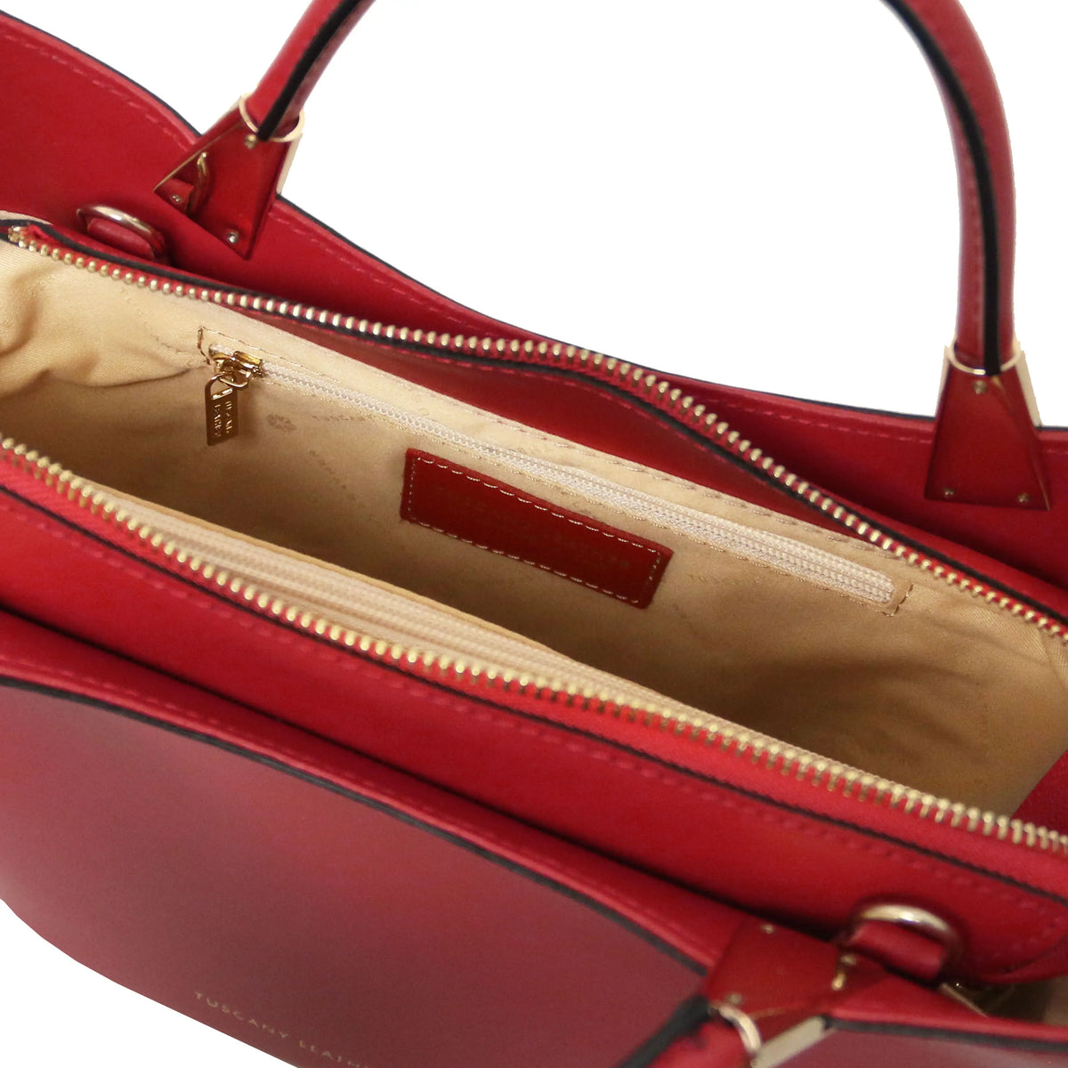 Close-up of a red leather handbag showing the open top interior with a beige zippered compartment, gold-tone zipper, and a small red interior label.
