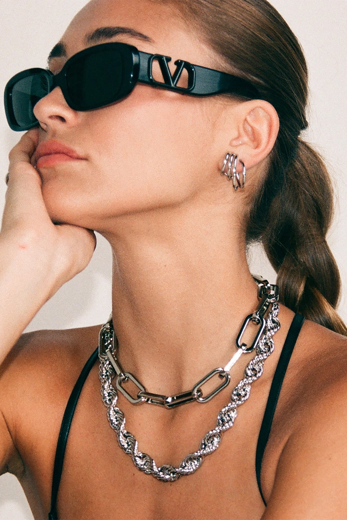 Woman wearing black sunglasses and a silver chain necklace with a white background
