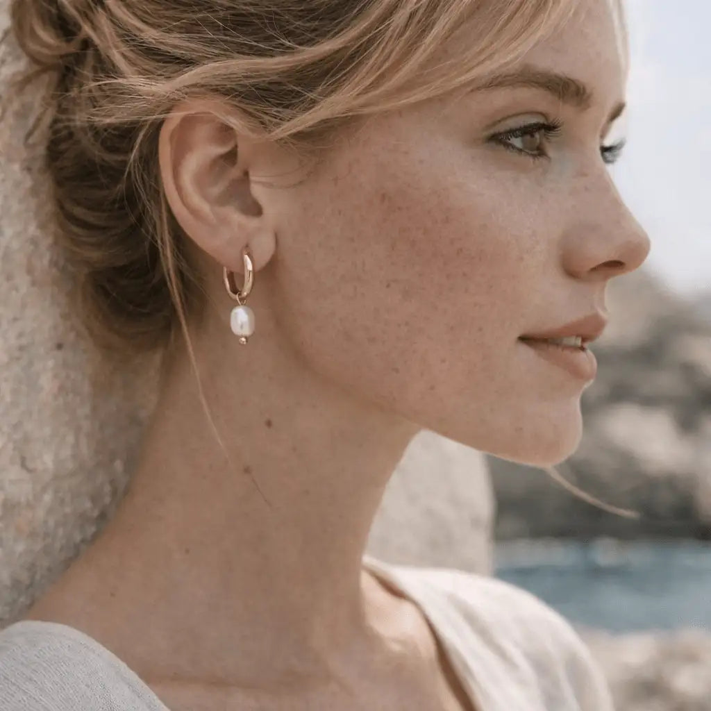 A woman is wearing the Villa D’Este Small Hoop Pearl Earrings on a natural background.