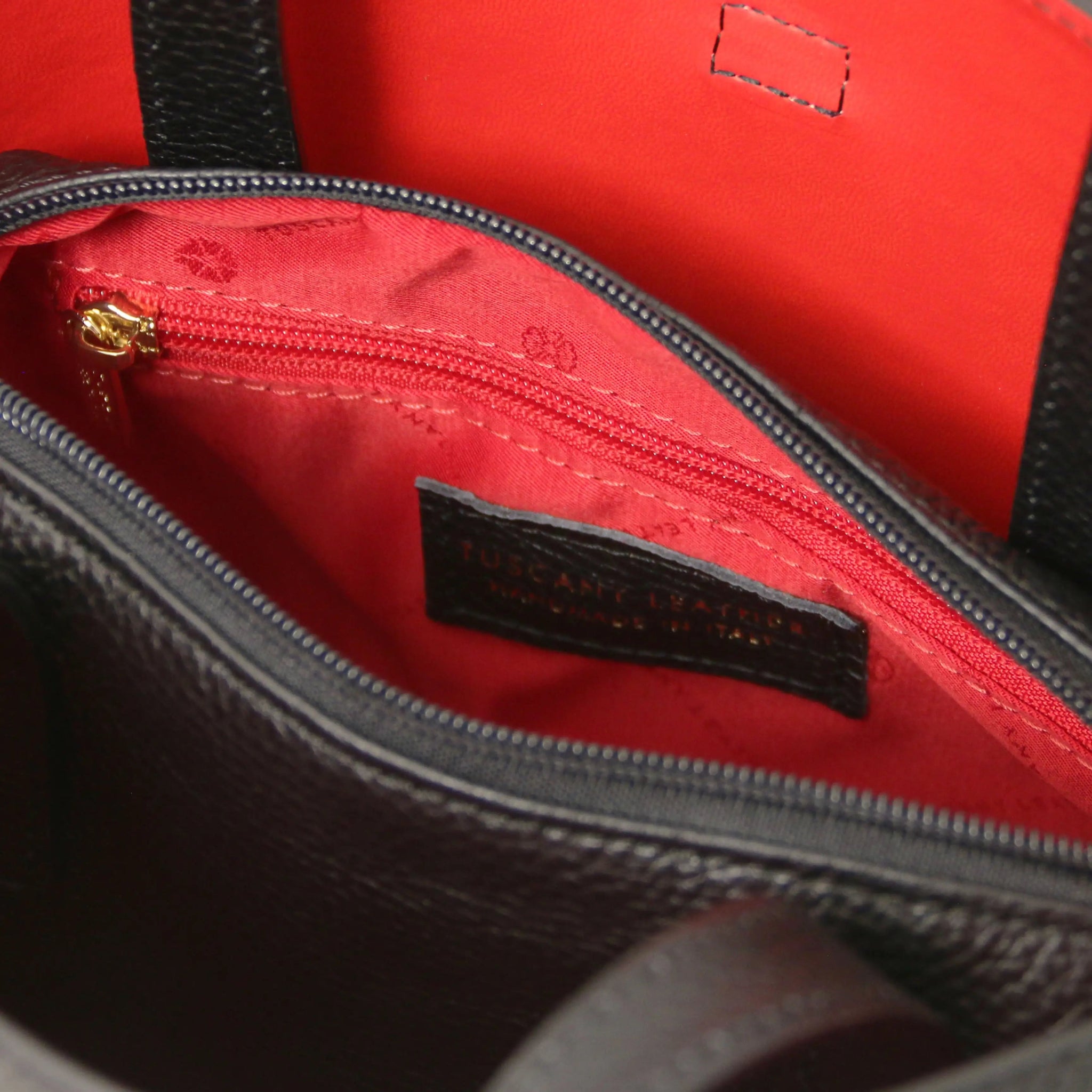 Close-up of a red interior of black bag with zip pocket and stitching details.