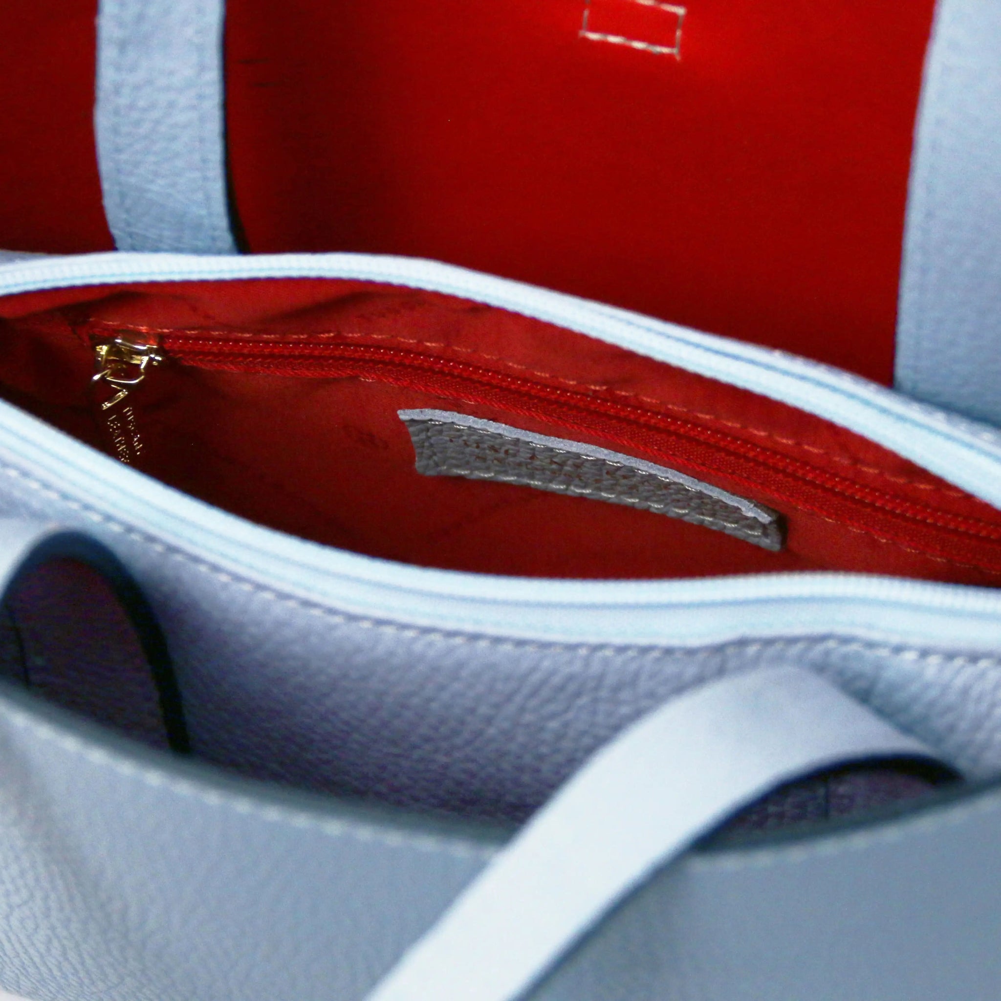 Close-up of light blue bag with red interior and a zippered compartment.