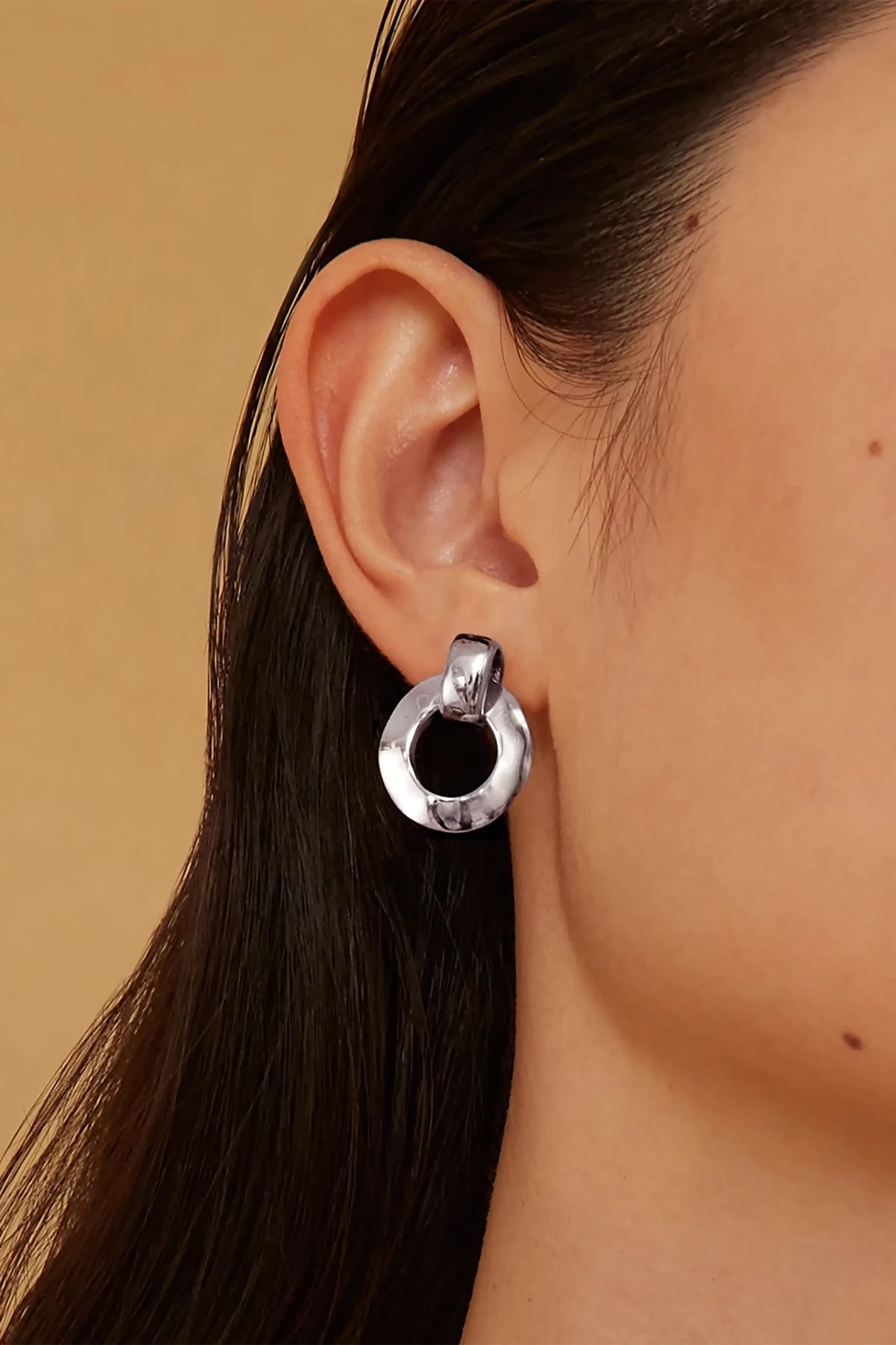 Silver hoop earring worn by a woman with a neutral background
