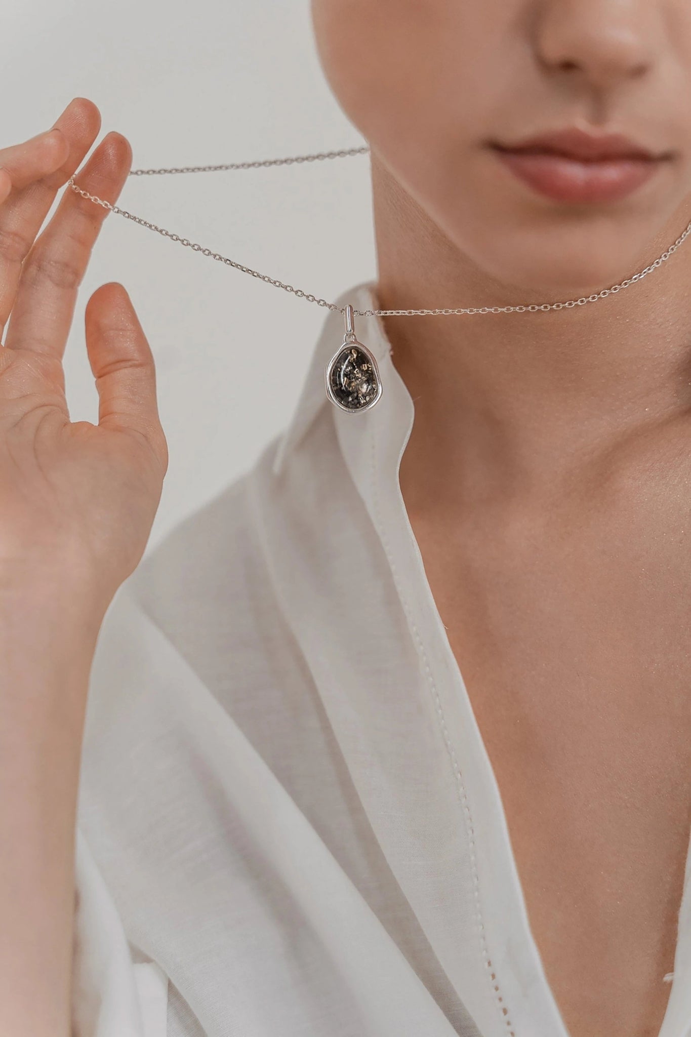 A female model is holding the Baltic Green Amber Element Silver Pendant Necklace