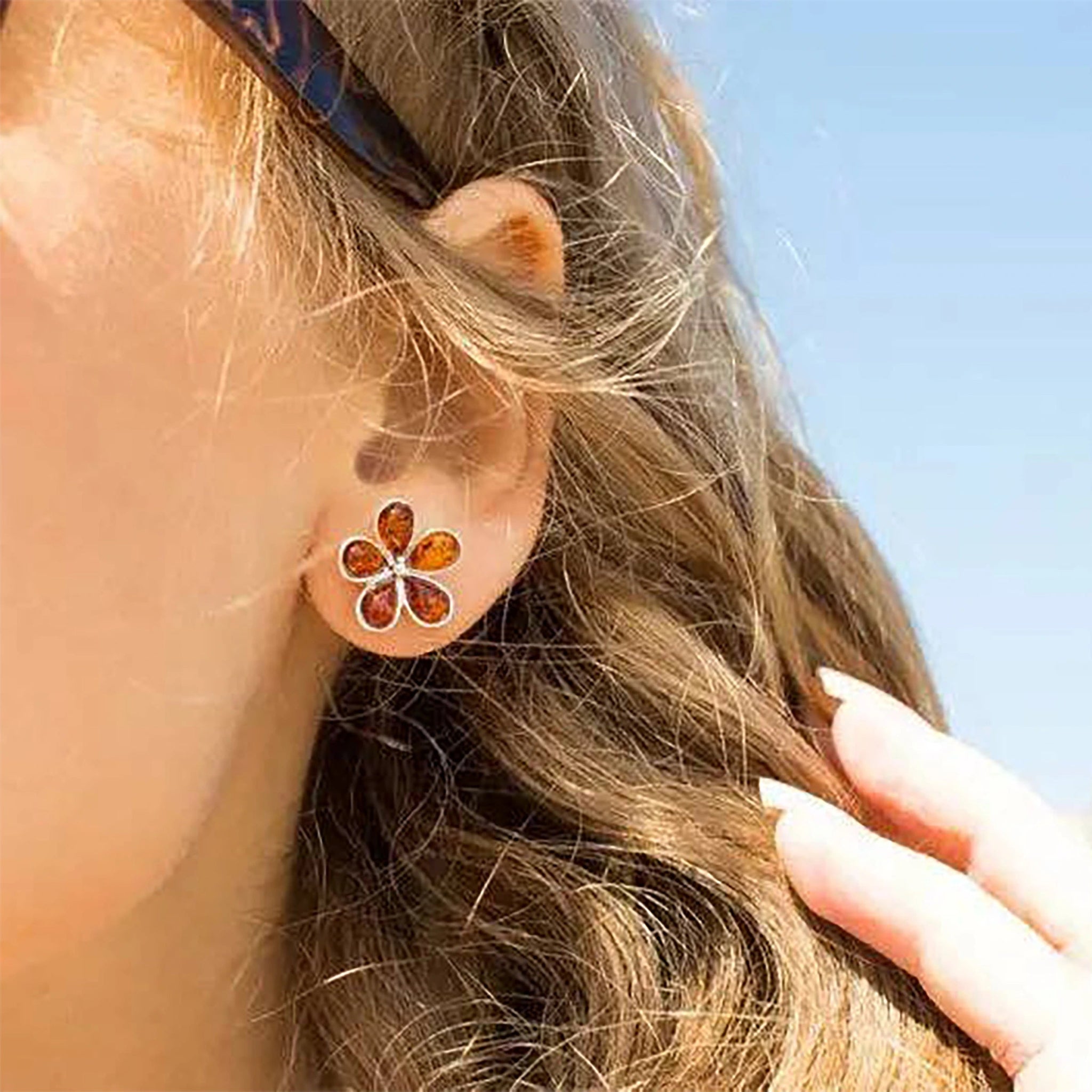 Female model wearing Baltic Honey Amber Daisy Silver Stud Earrings outside. The amber gem is glistening in the light.