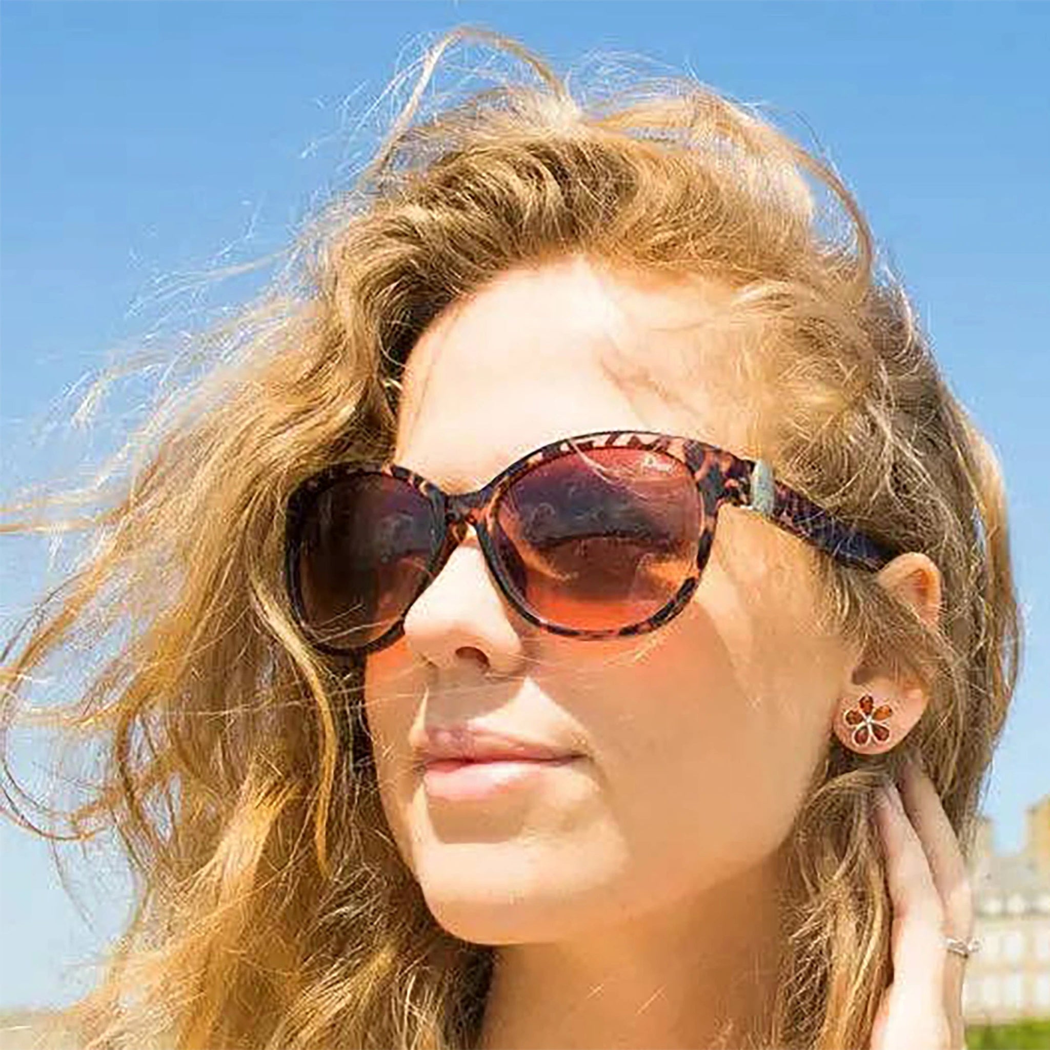 A female model wearing Baltic Honey Amber Daisy Silver Stud Earrings outside. The amber gem is glistening in the light.