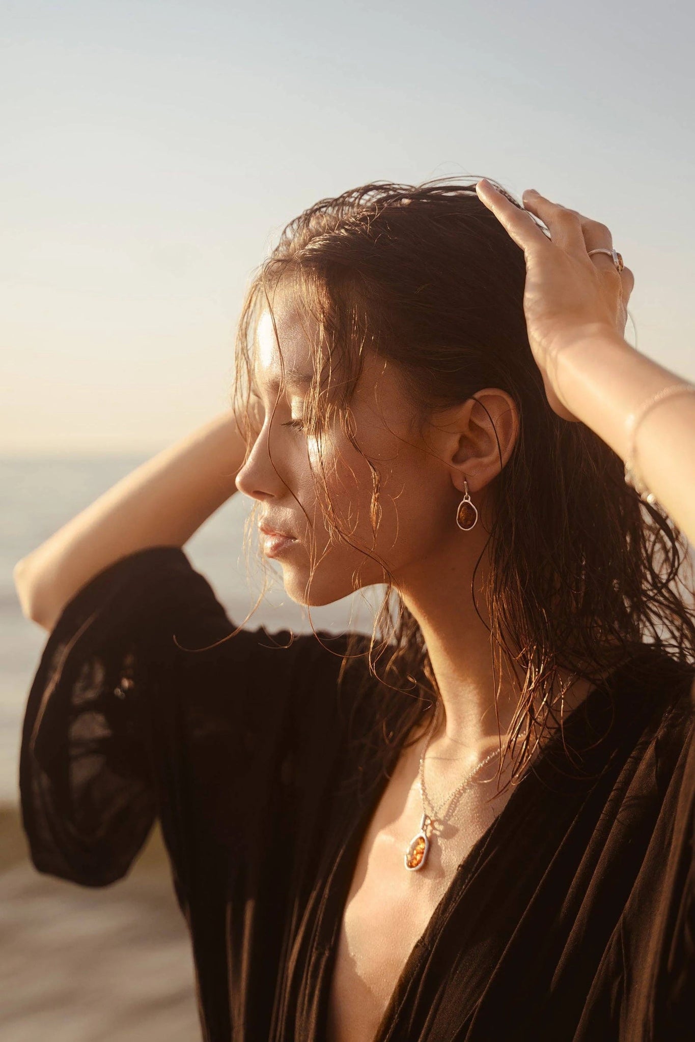 A woman is outside wearing the Baltic Honey Amber Element Pendant Necklace and drop earrings that are glistening in the sun.