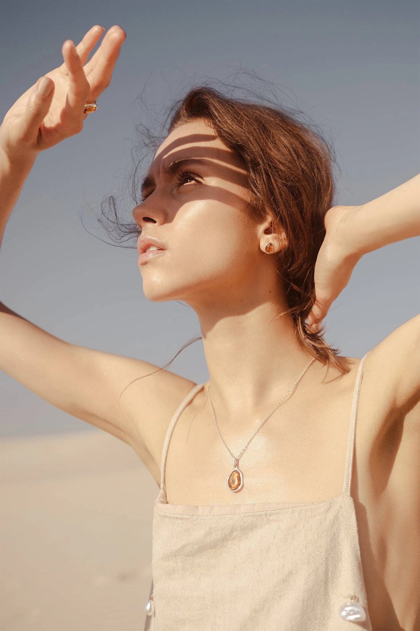 A woman is outside wearing the Baltic Honey Amber Element Pendant Necklace and drop earrings that are glistening in the sun.