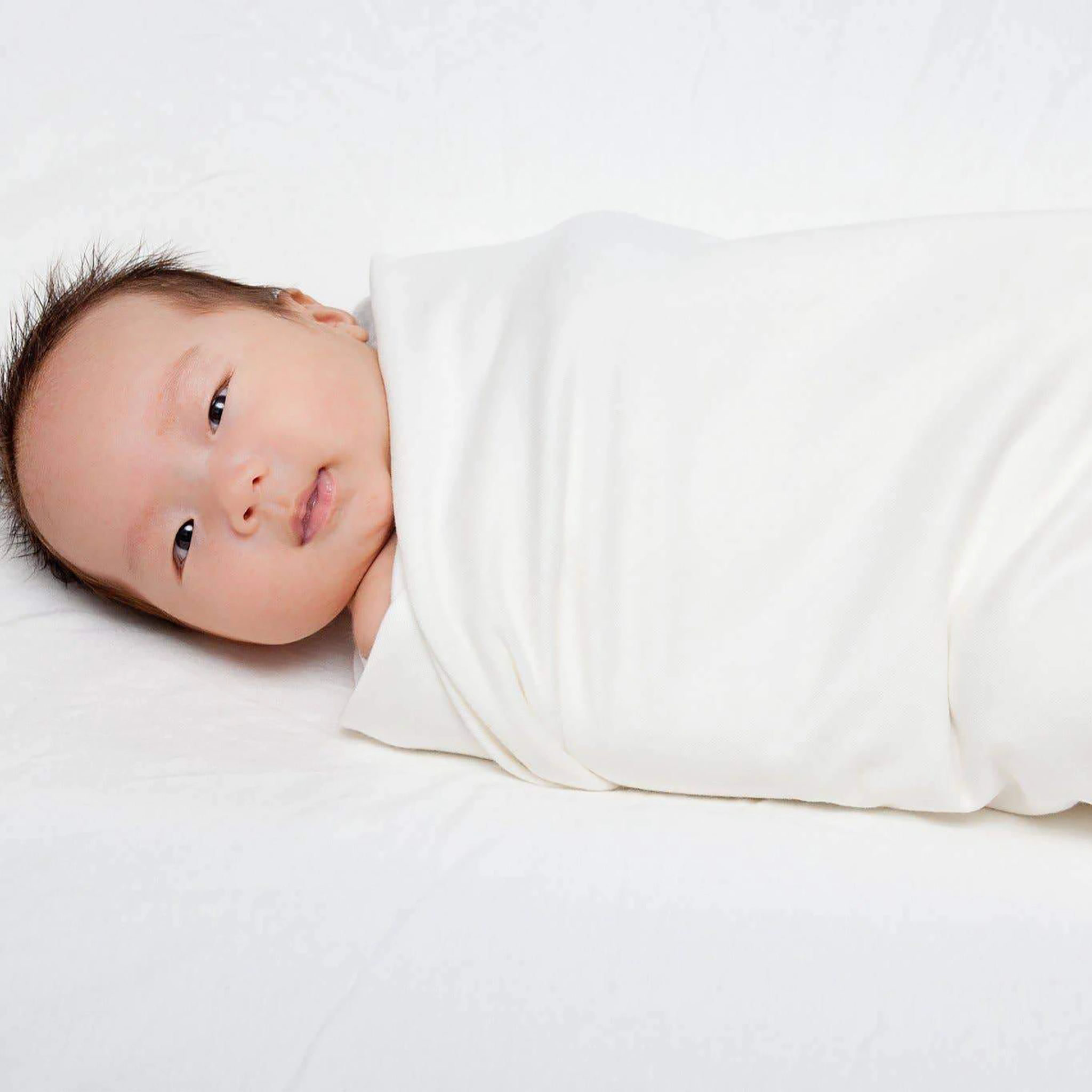 Newborn baby wrapped in a white blanket on a light background