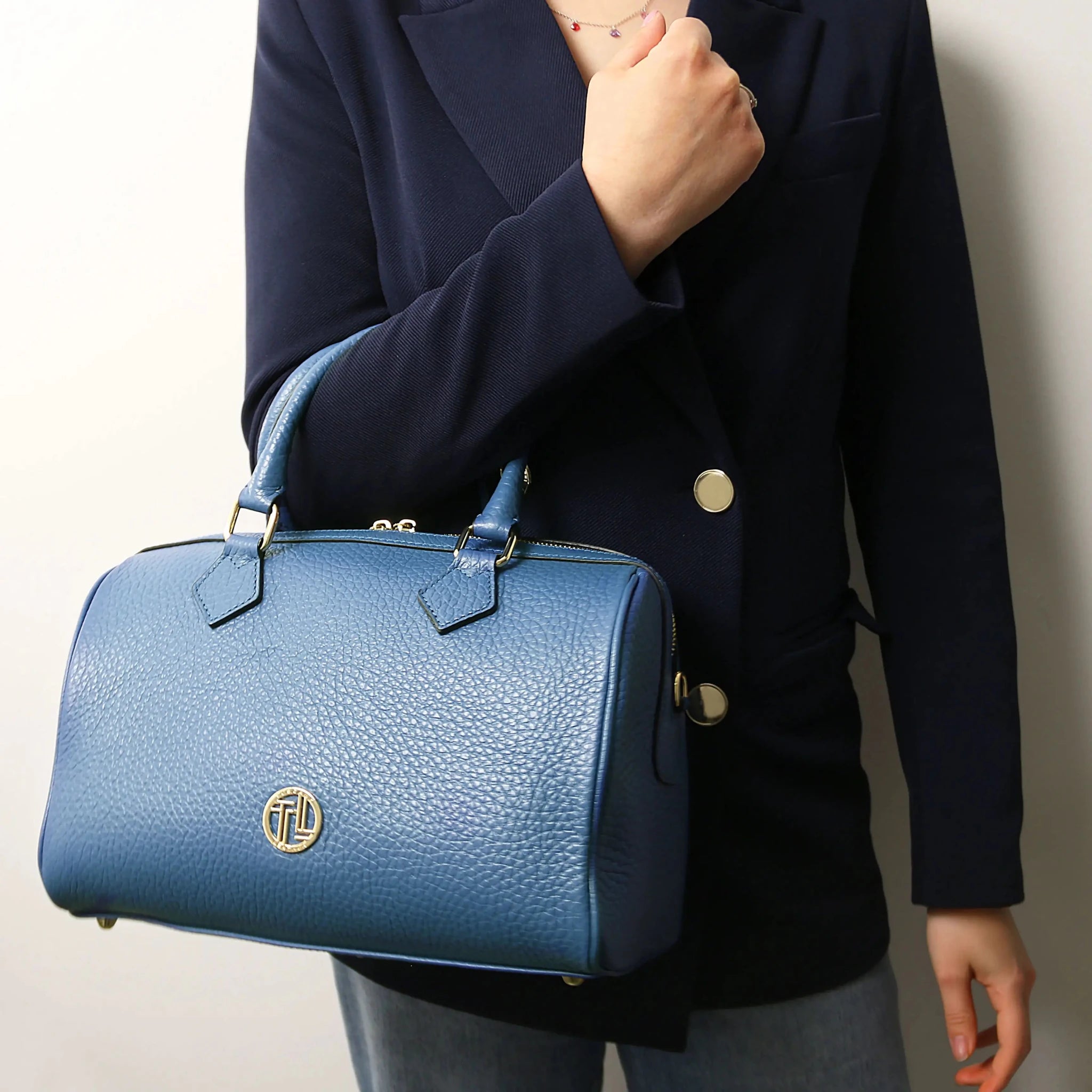 Person holding a blue handbag with a visible brand logo against a neutral background