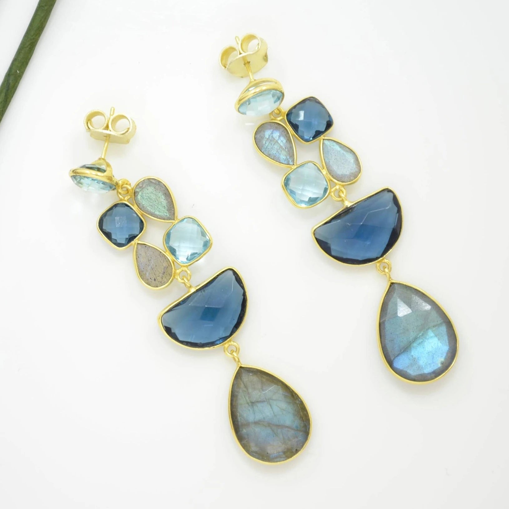 Close up pair of blue gemstone earrings with gold accents on a natural background
