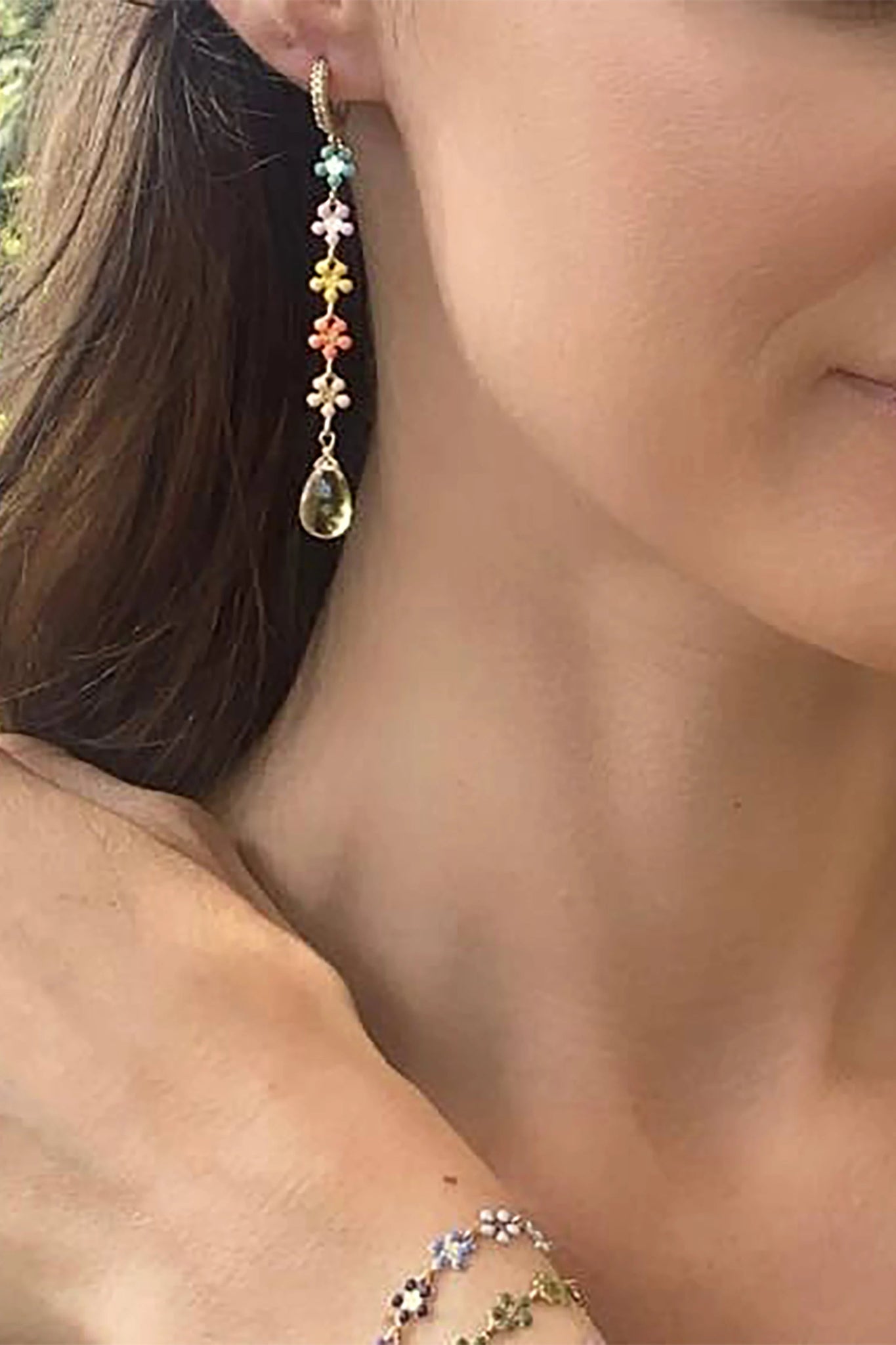 A model is showcsing the Blue Topaz Daisy Huggie Dangle Earrings on her right ear set in front of her brown hair.