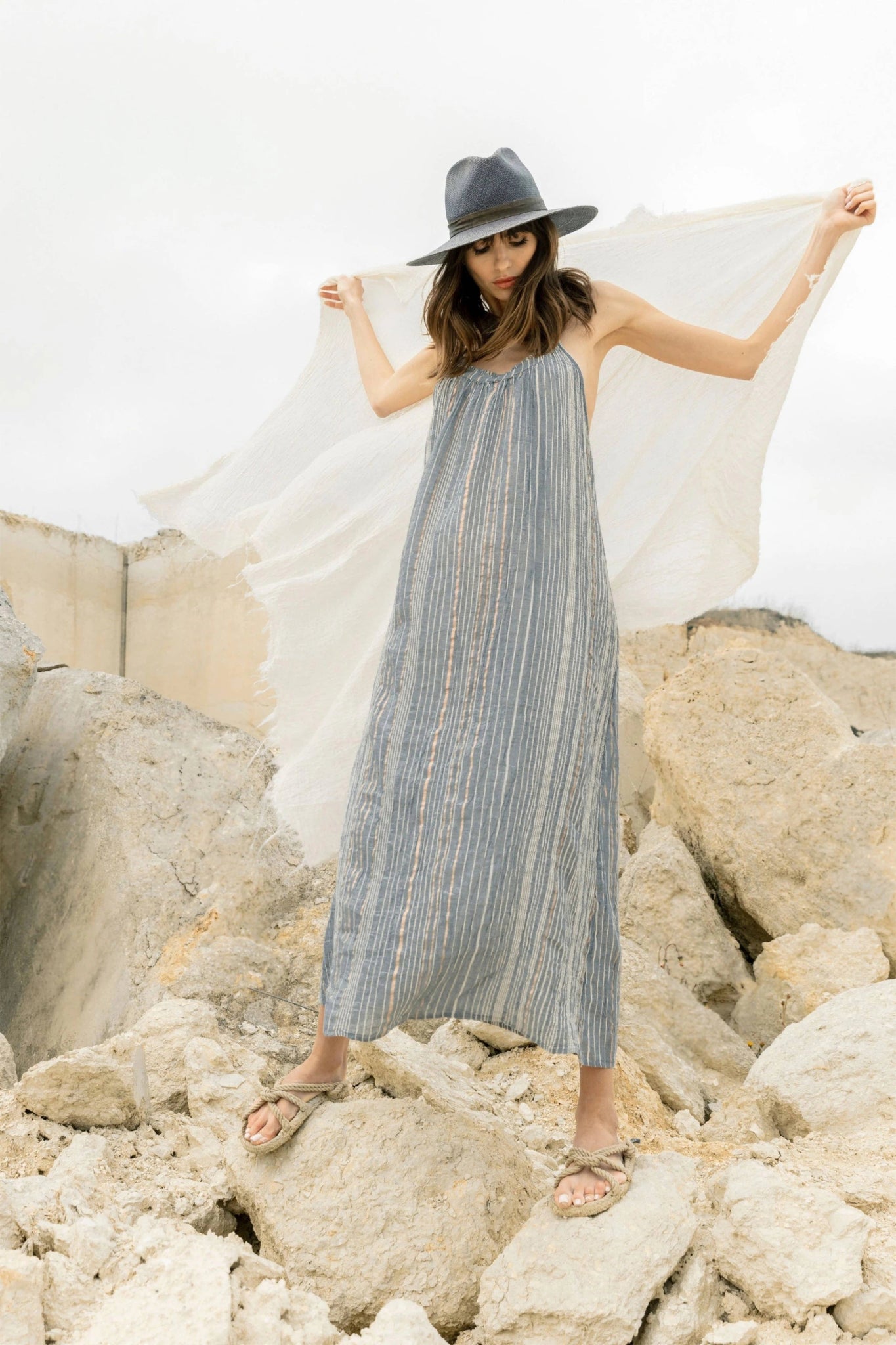 Woman in a long striped navy dress and hat standing on rocky terrain with a white cloth.