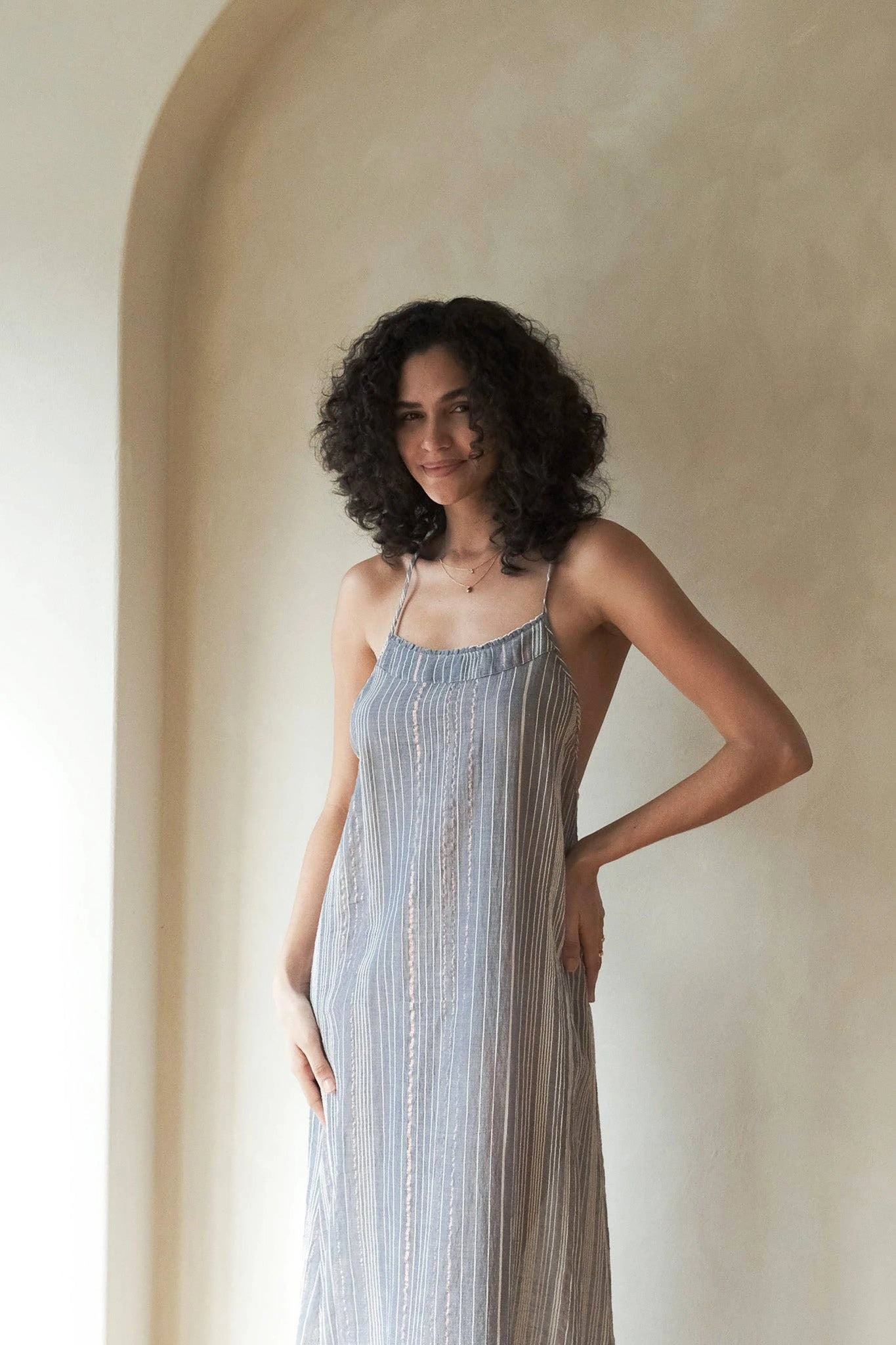 Woman wearing a striped dress standing against a neutral wall.