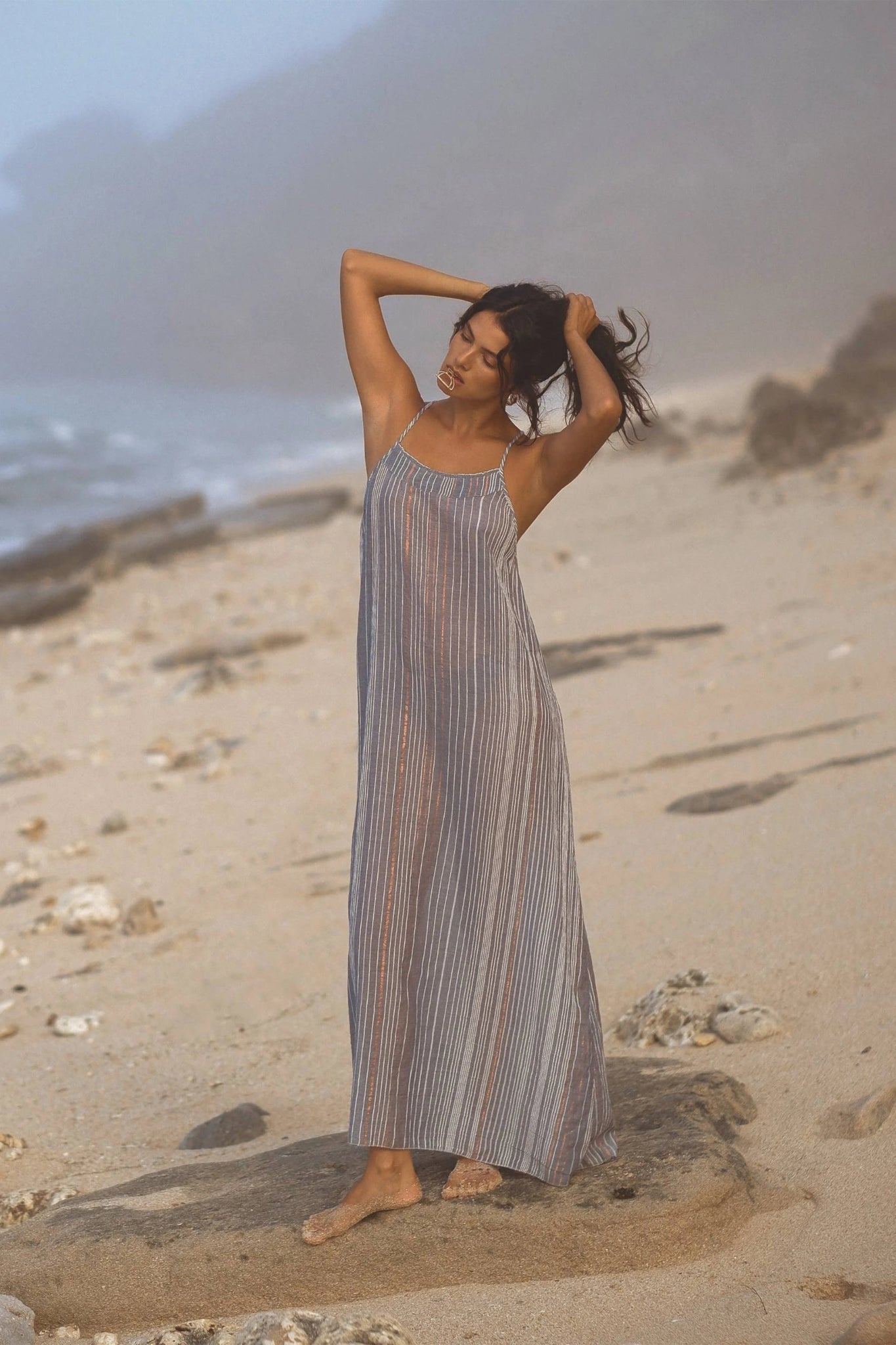 Woman in a striped dress standing on a beach with ocean in the background