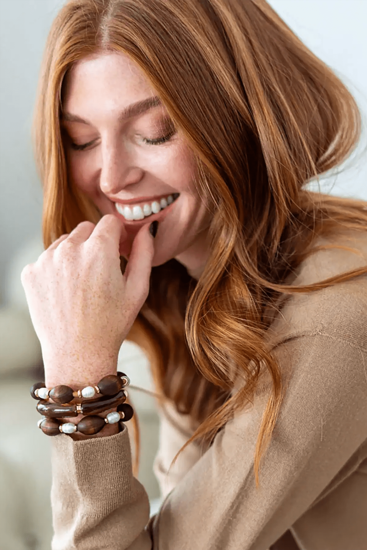 Woman wearing multiple bracelets on her wrist, smiling with hand near mouth.