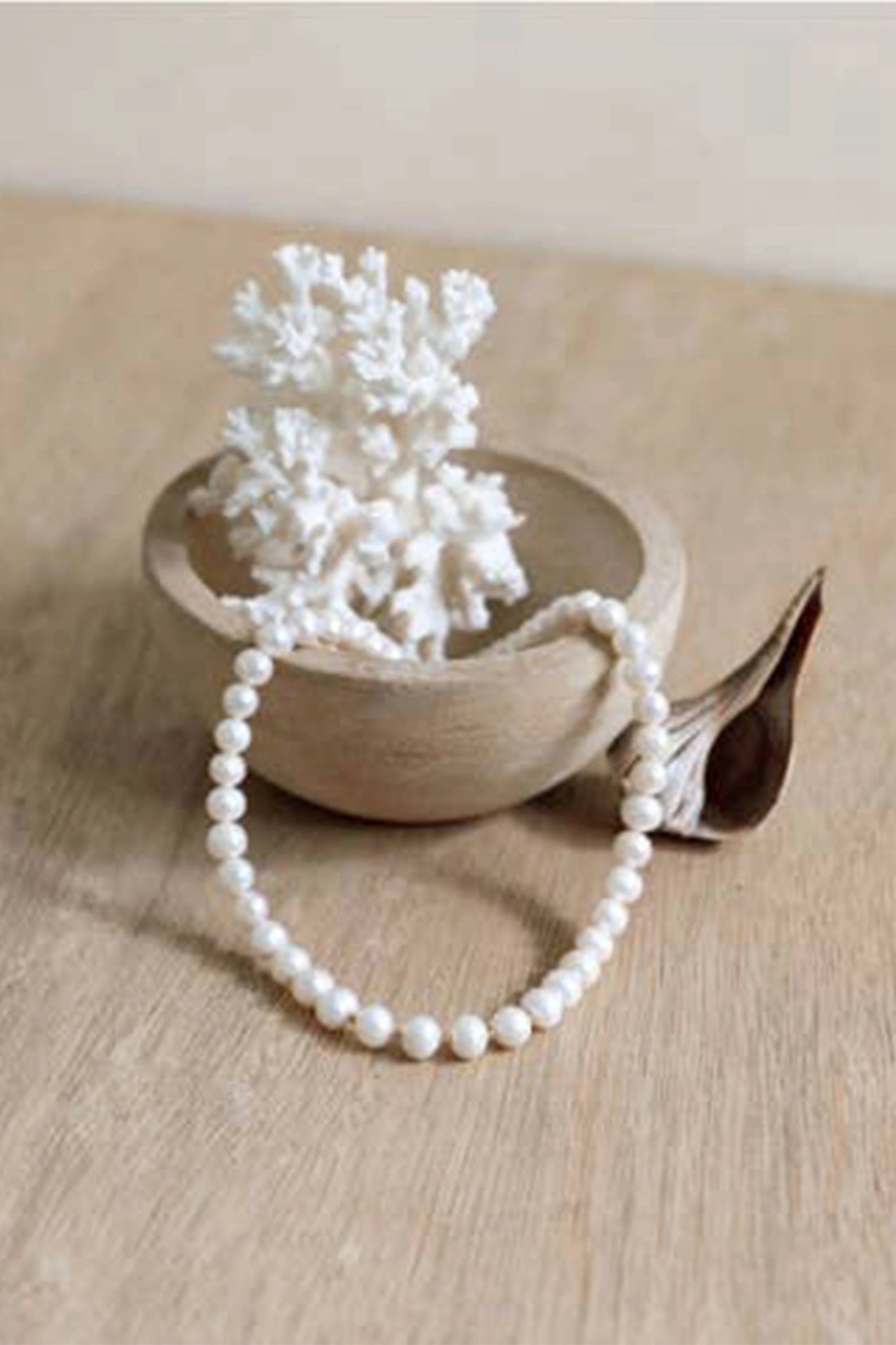 Cassis Golden Pearl Necklace partially laying inside a bowl near a white coral in a all natural beige setting