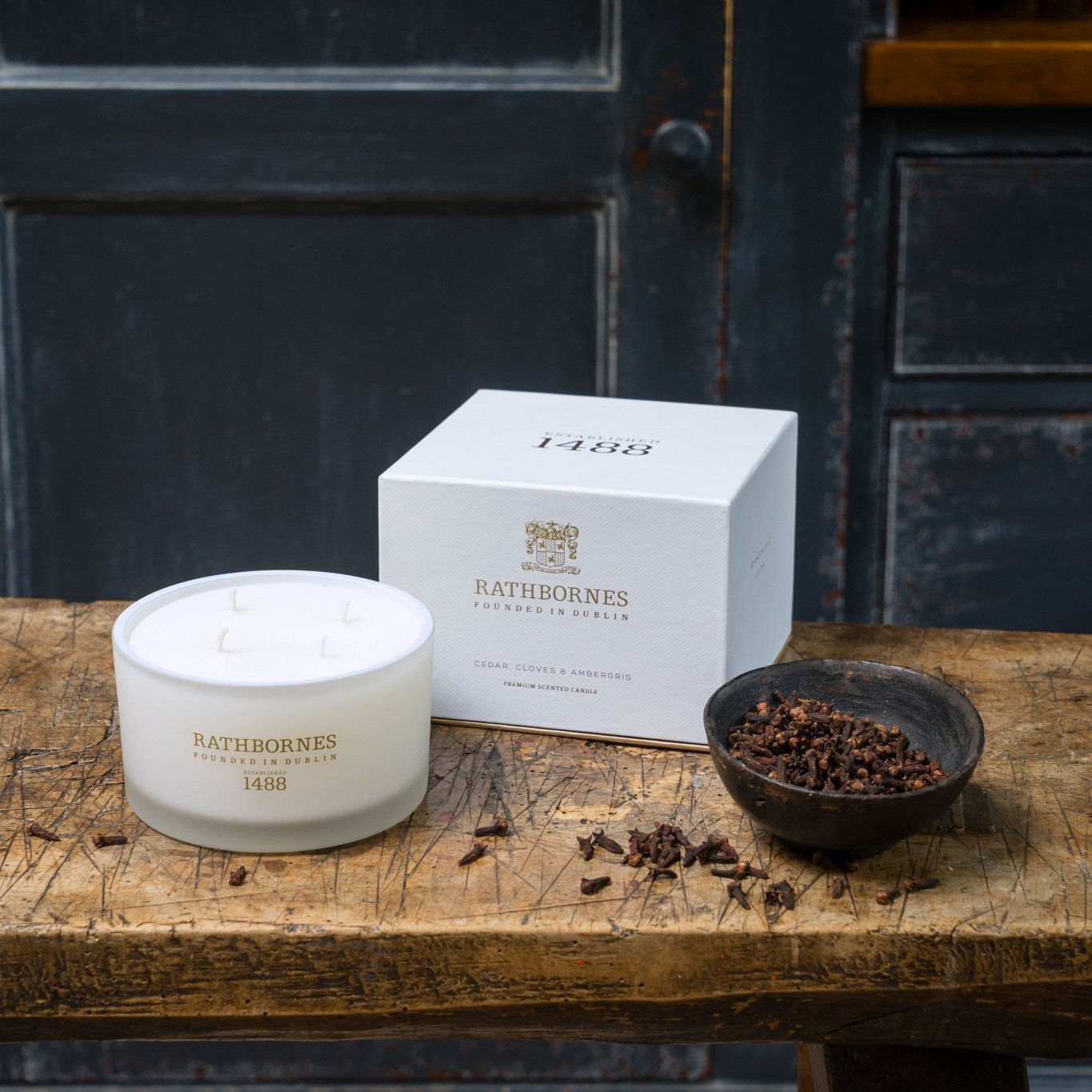 Cedar Cloves & Ambergris Luxury Beeswax Irish Candle o a wooden table near crushed cloves in bowl