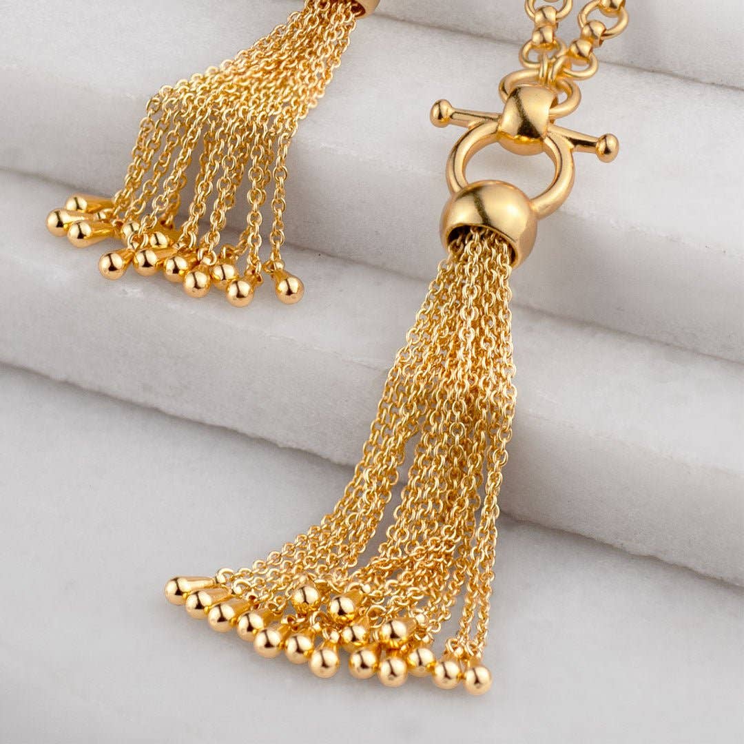 Gold necklace with tassel pendant on a light gray surface