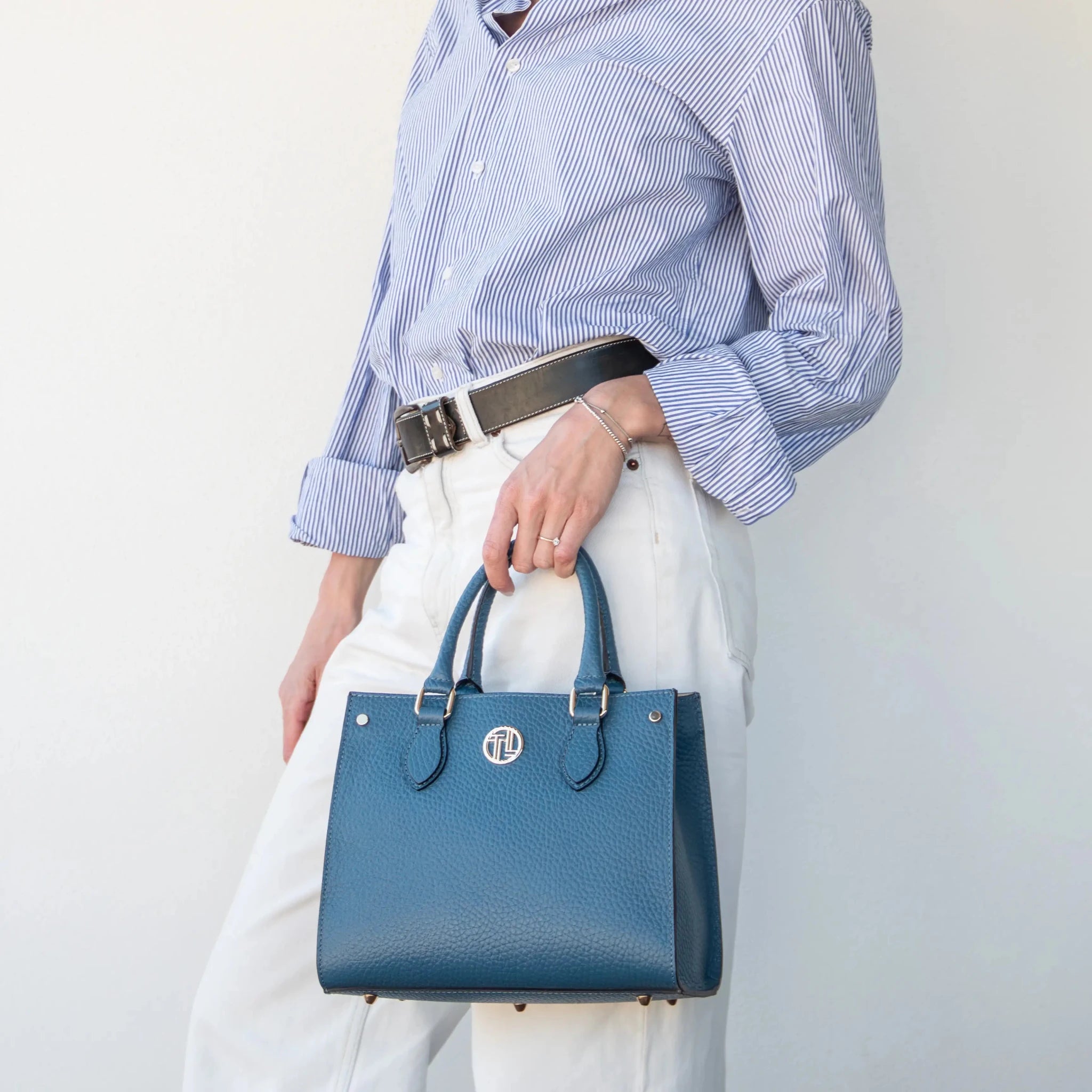 Woman wearing white pants hlodling the Croque Italian Pebbled Leather Handbag in blue