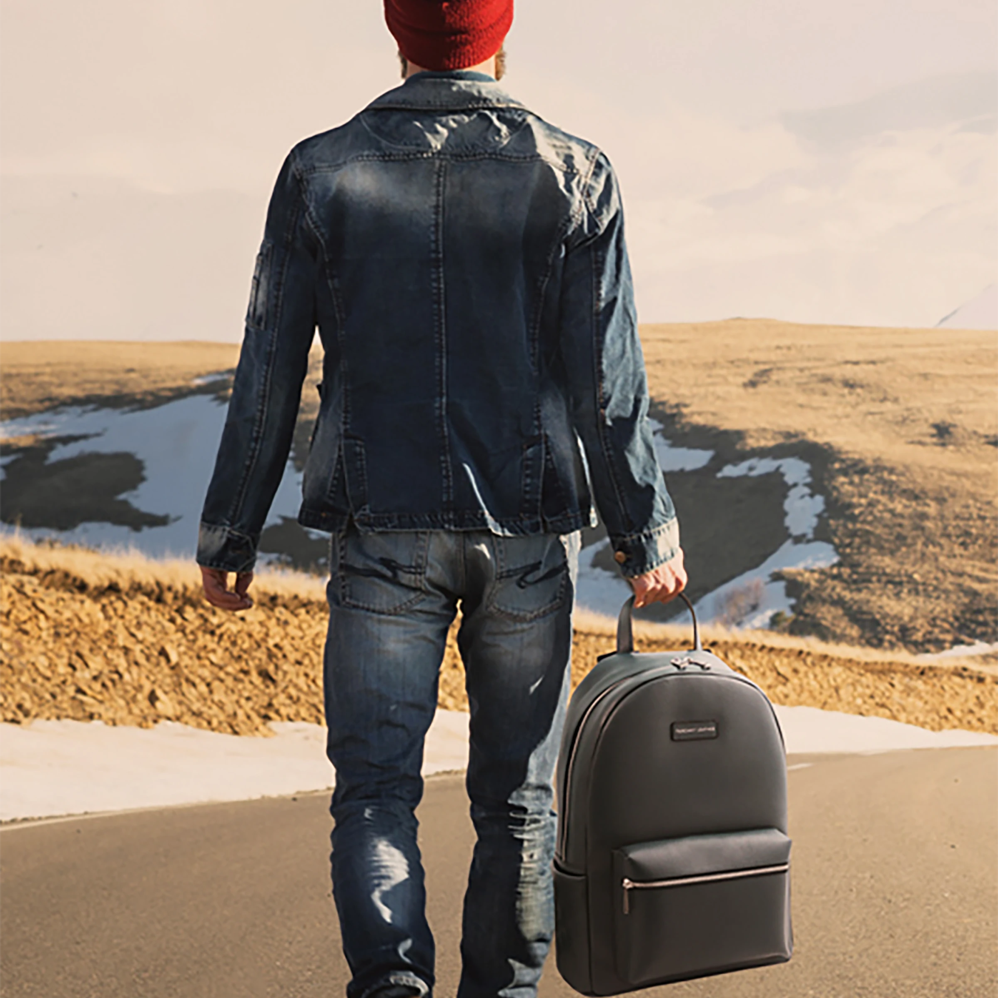 Model wearing jean jacket and pants wearing a red knit hat holding the Dakota Soft Italian Leather Backpack