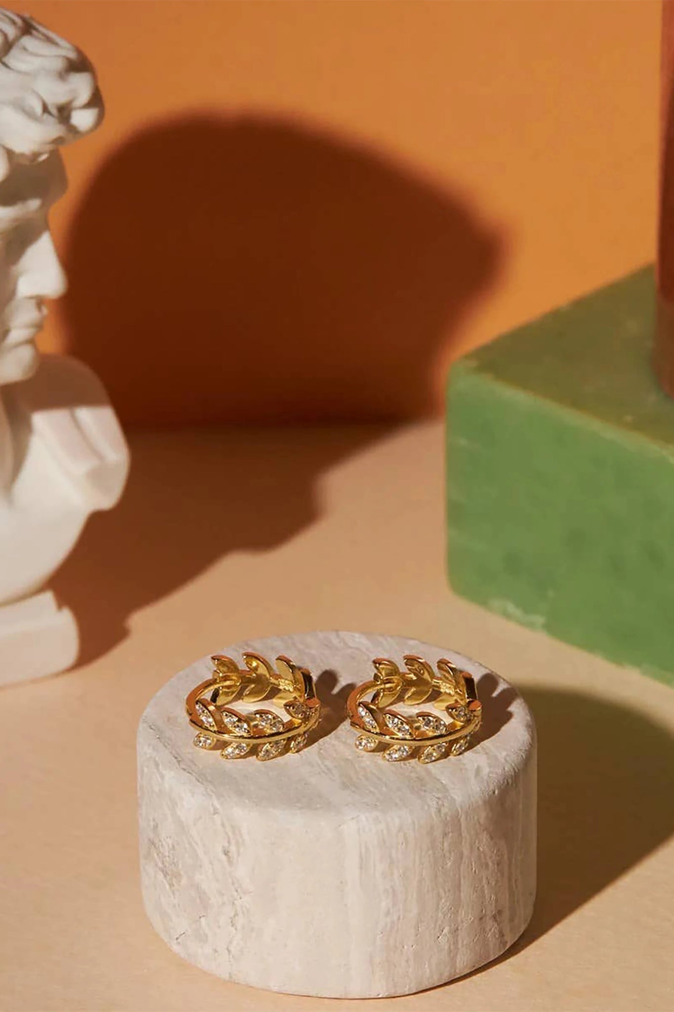 Dancing Leaves Cubic Zirconia Huggie Hoop Earrings in Gold laying on a stone circular stand.