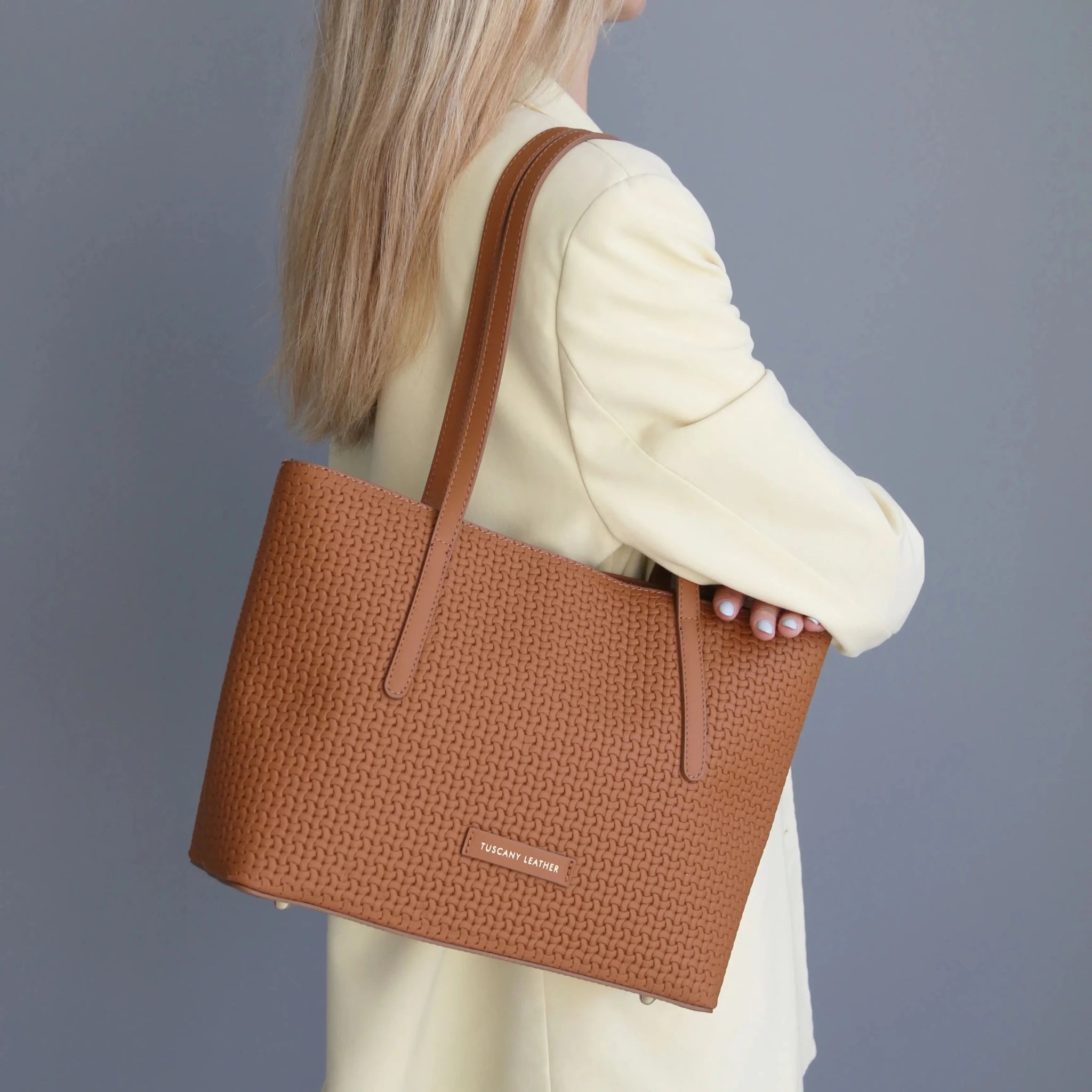 Woman in ivory suit jacket holding the Dedalo Woven Leather Shopping Bag in cognac