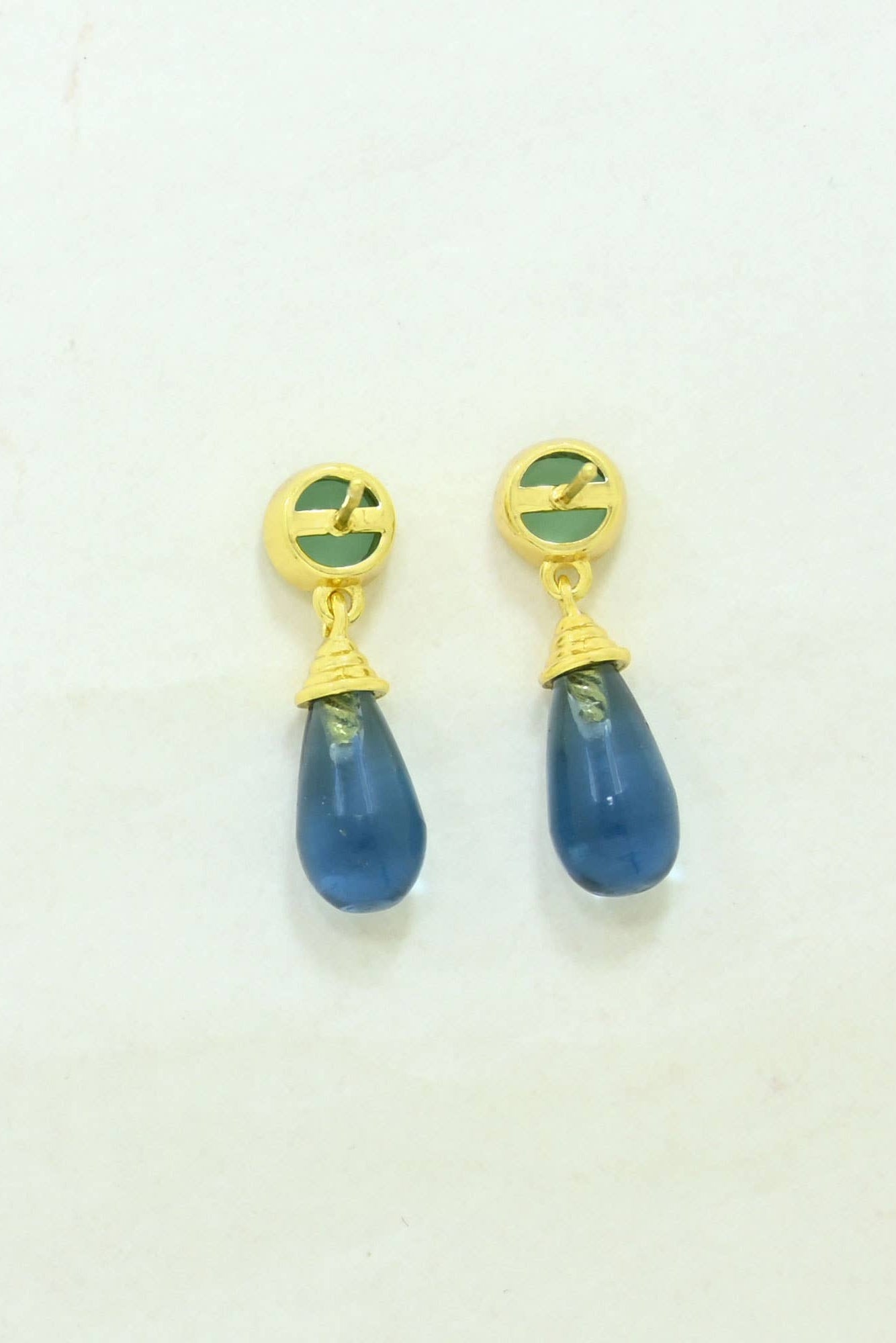 Pair of earrings with gold tops, green accents, and blue teardrop-shaped drops on a light beige background.