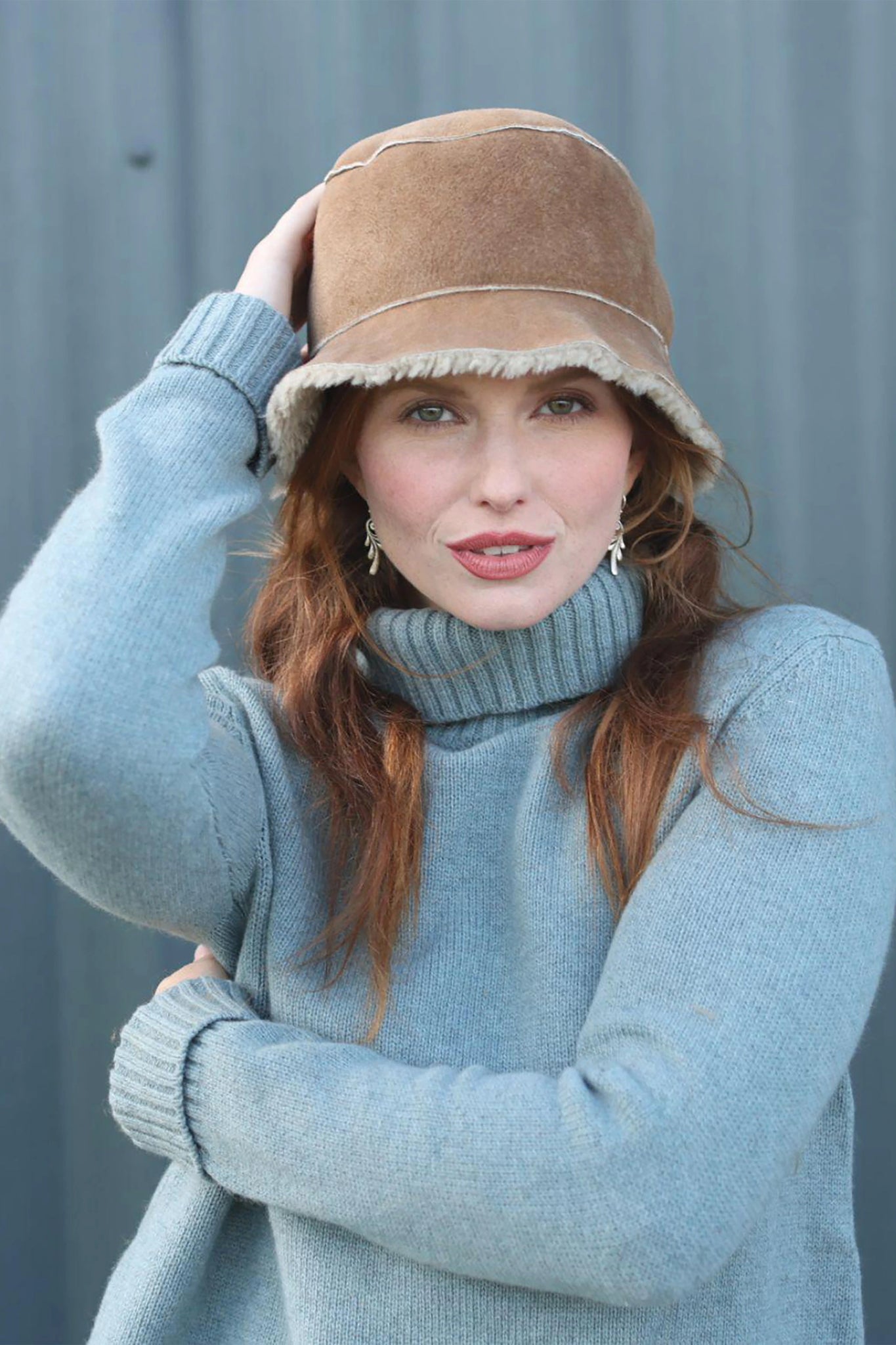 Front view English Sheepskin Bucket Hat in Tan Gonfio on a model wearing a light blue turtleneck sweater. The rim touches the top of her eyebrows
